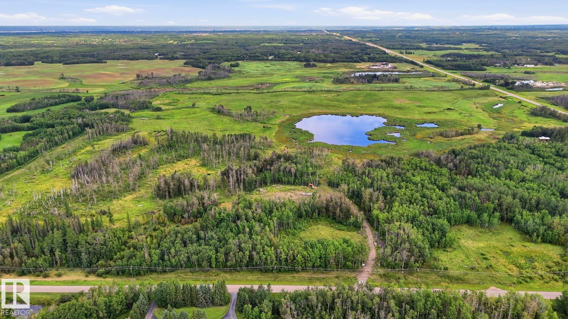 Extensive acreage featuring a natural pond, lush green fields, and mature tree coverage - 52012 Hwy 21, Rural Strathcona County, AB - Outdoor With View