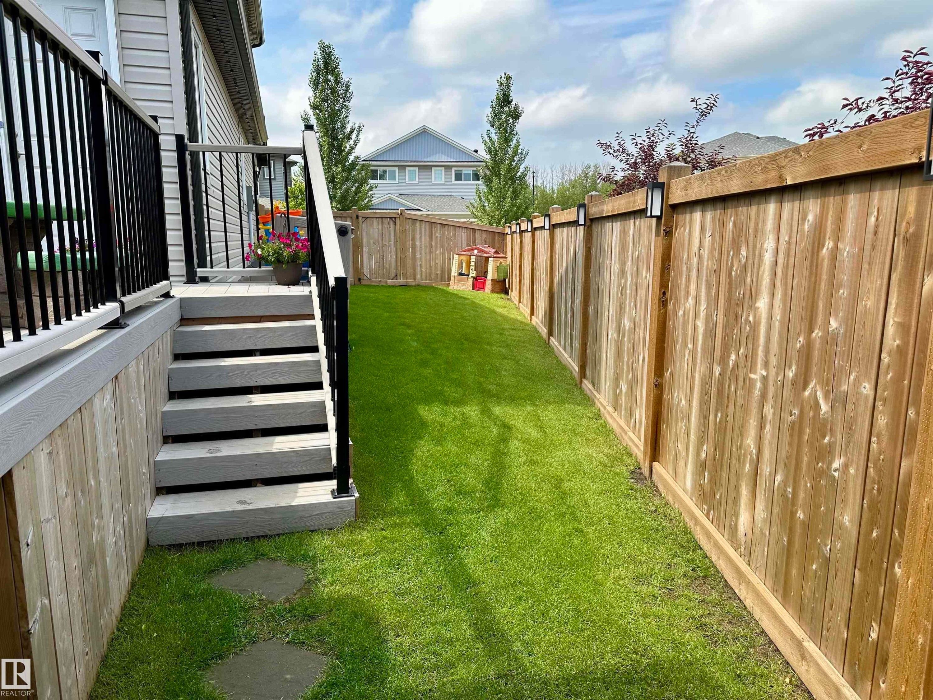 Expansive backyard featuring a manicured lawn, full privacy fencing with integrated lighting, and a composite deck with black metal railing - 17359 49 Street Nw, Edmonton, AB - Outdoor