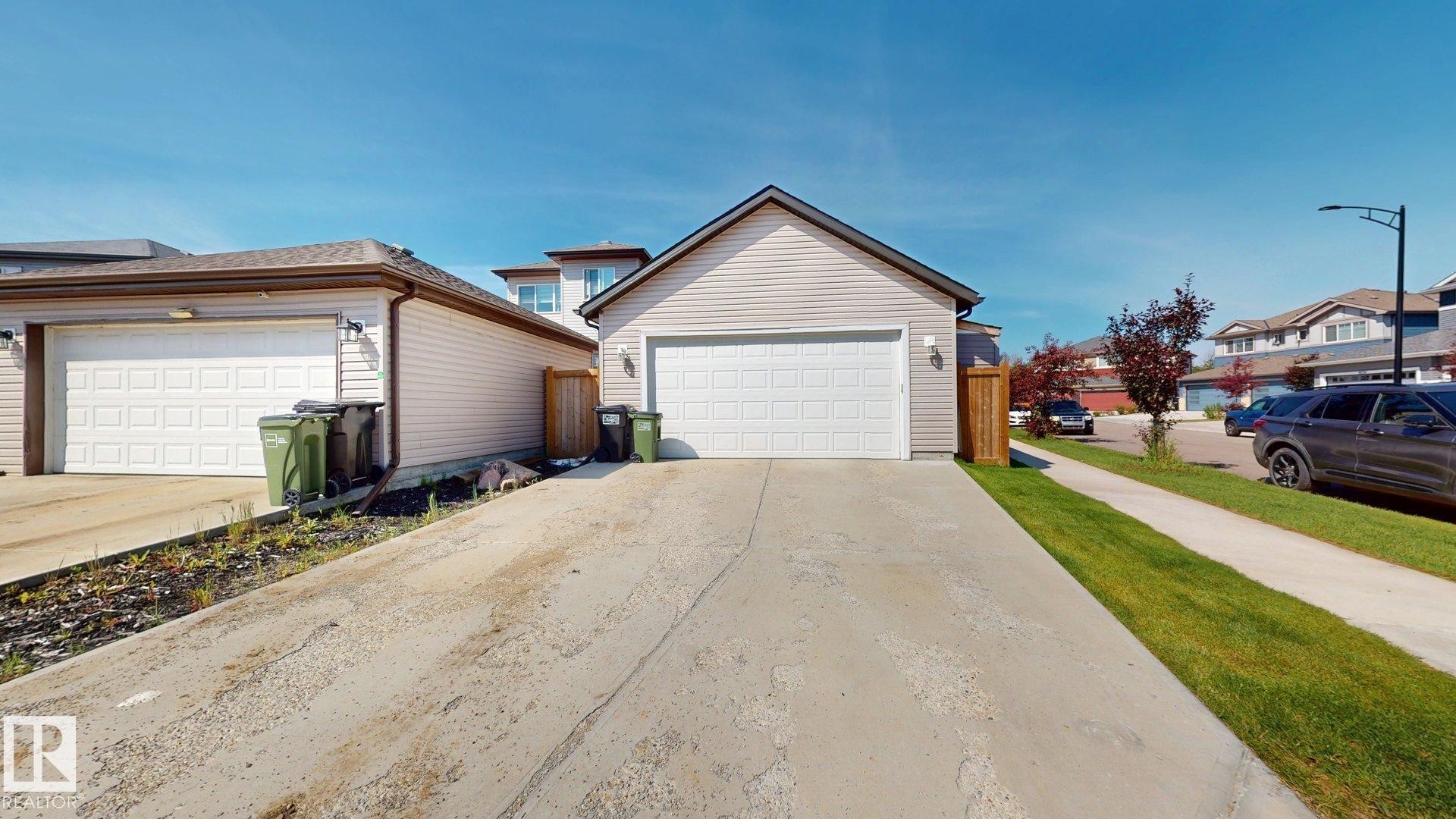 Welcoming front elevation featuring a spacious two-car garage with white panel doors, neutral siding exterior, and a wide concrete driveway - 17359 49 Street Nw, Edmonton, AB - Outdoor