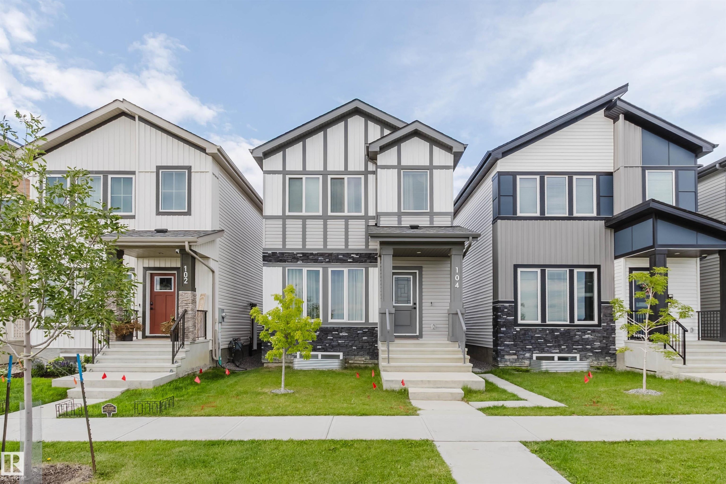 Modern gray and white exterior featuring dark trim accents, multiple windows, a covered entry, and concrete steps - 104 Meadowview Way, Leduc, AB - Outdoor With Facade