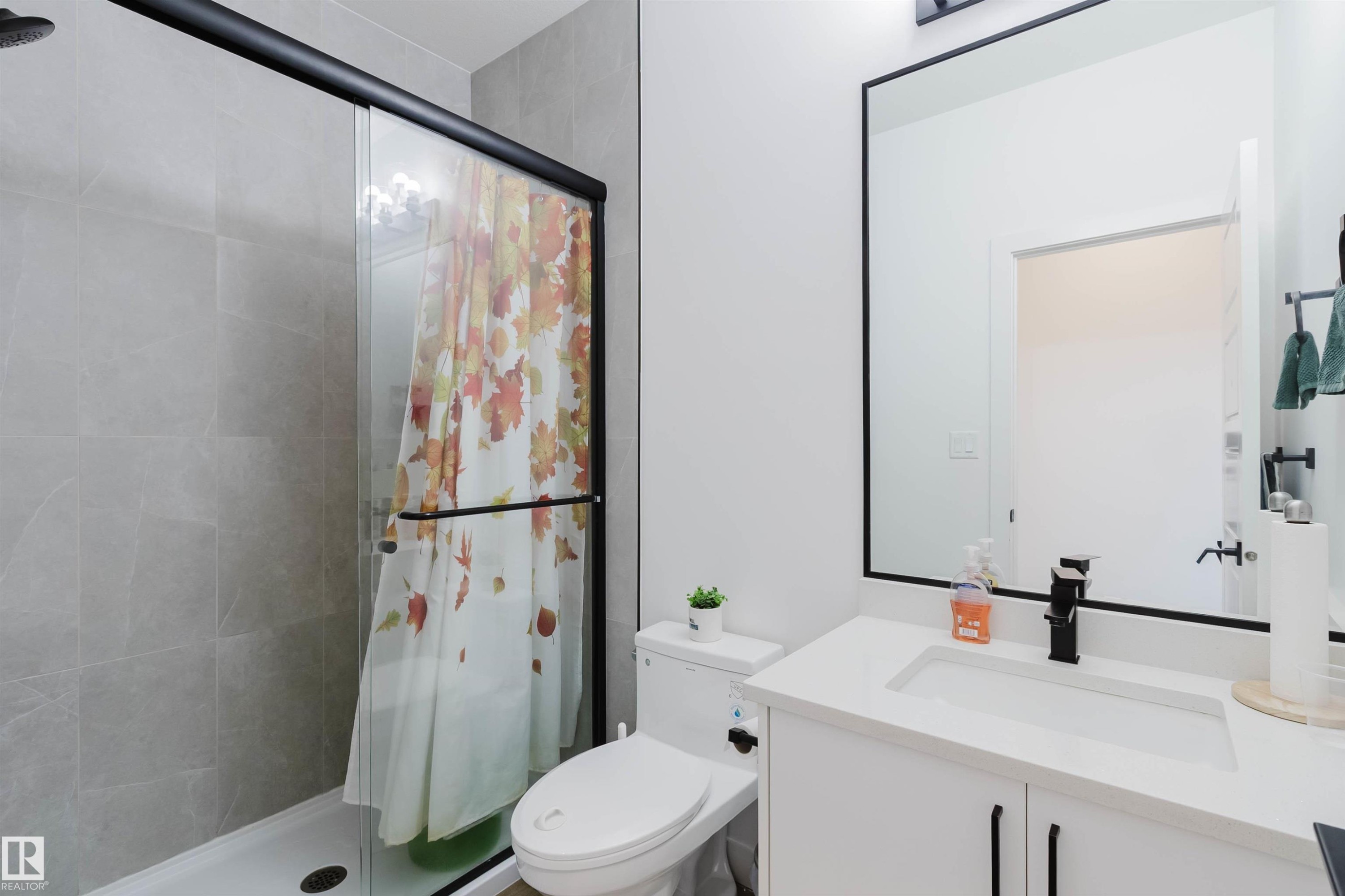 Glass-enclosed shower with black-framed sliding door and stone-finish wall tile - 104 Meadowview Way, Leduc, AB - Indoor Photo Showing Bathroom