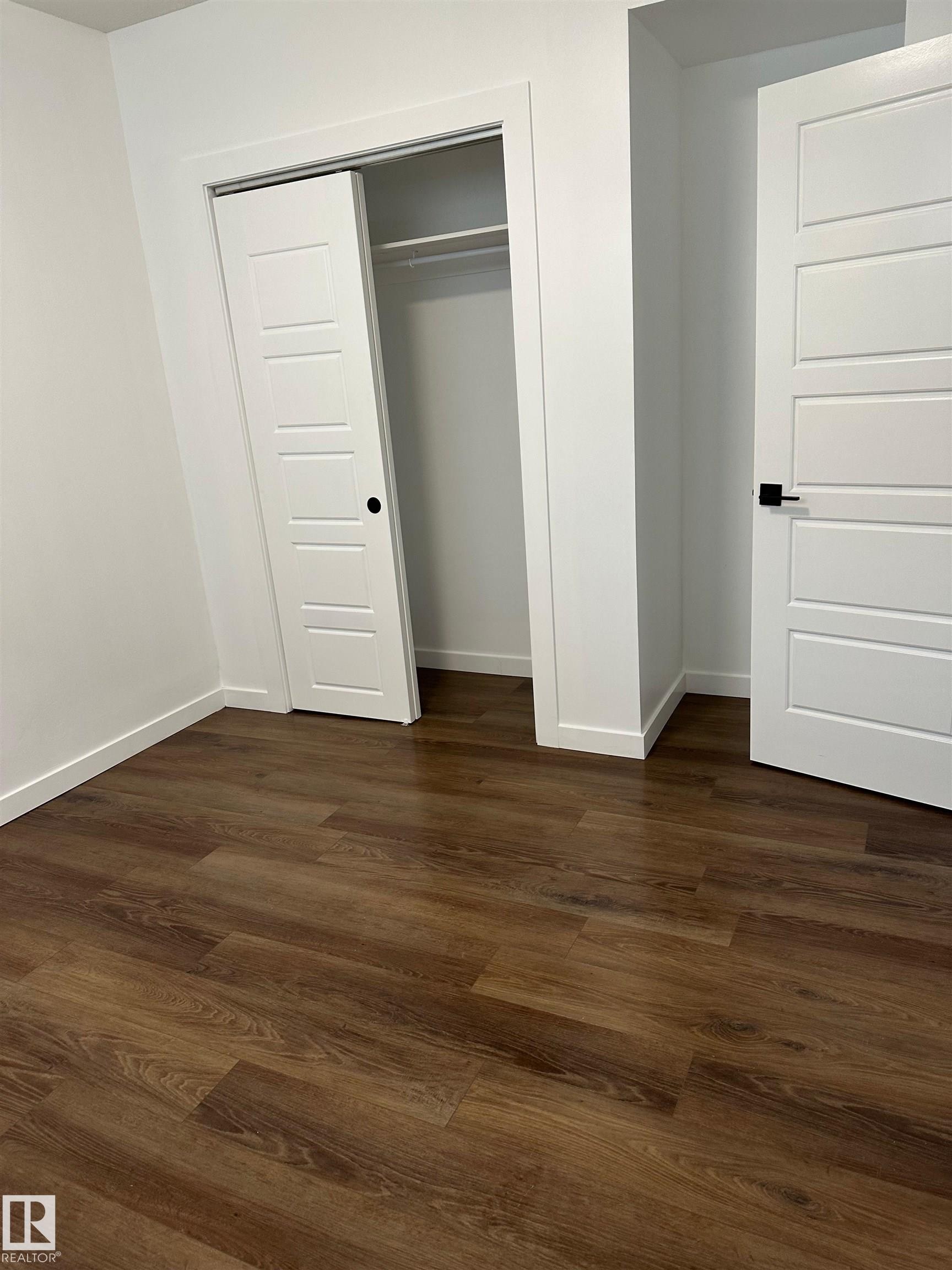 Wood-finish flooring, white paneled doors, sliding closet door with hanging rod, and white trim - 104 Meadowview Way, Leduc, AB - Indoor Photo Showing Other Room