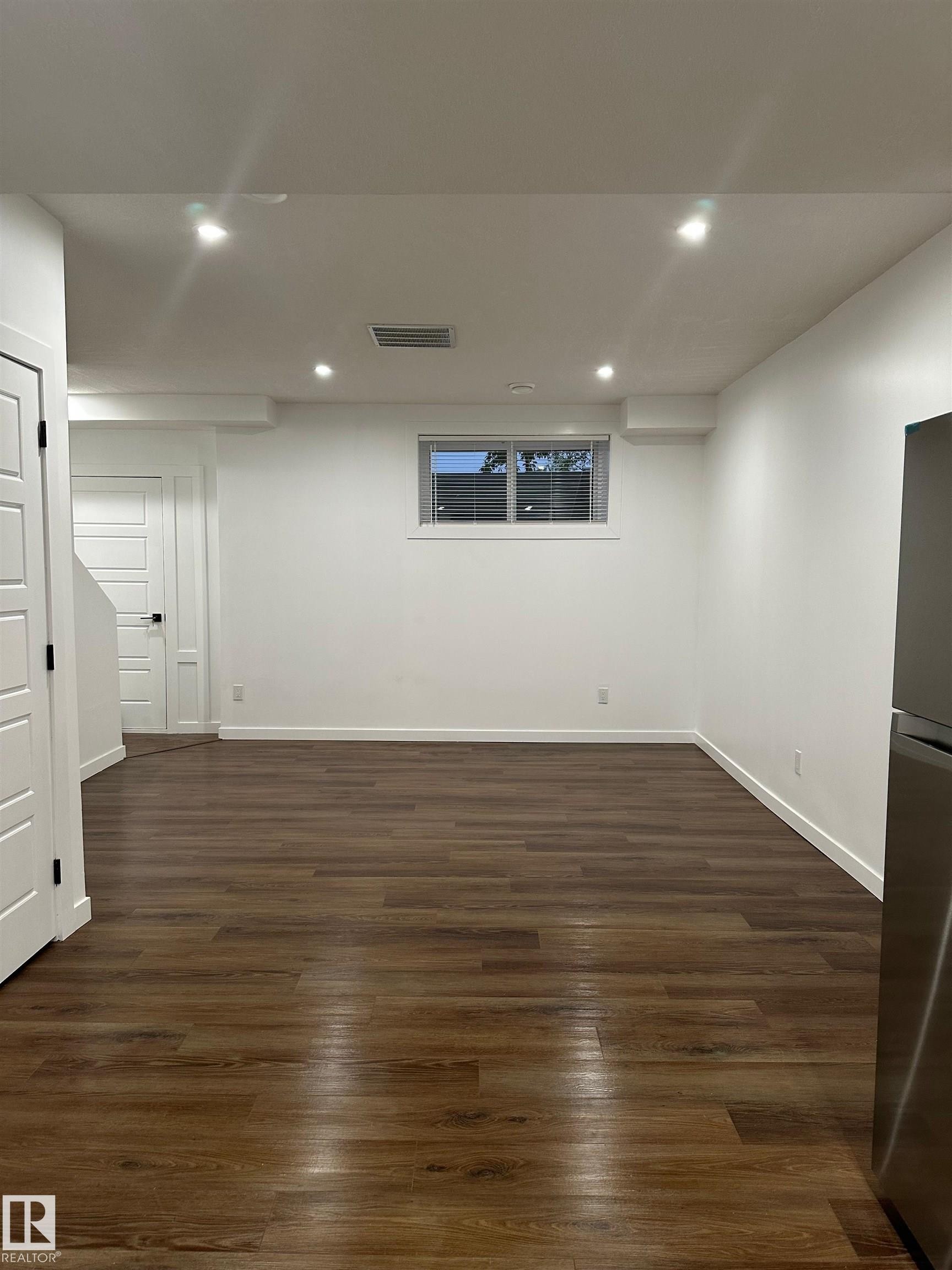 Spacious room with wood-finish flooring, recessed ceiling lighting, and a white paneled door - 104 Meadowview Way, Leduc, AB - Indoor