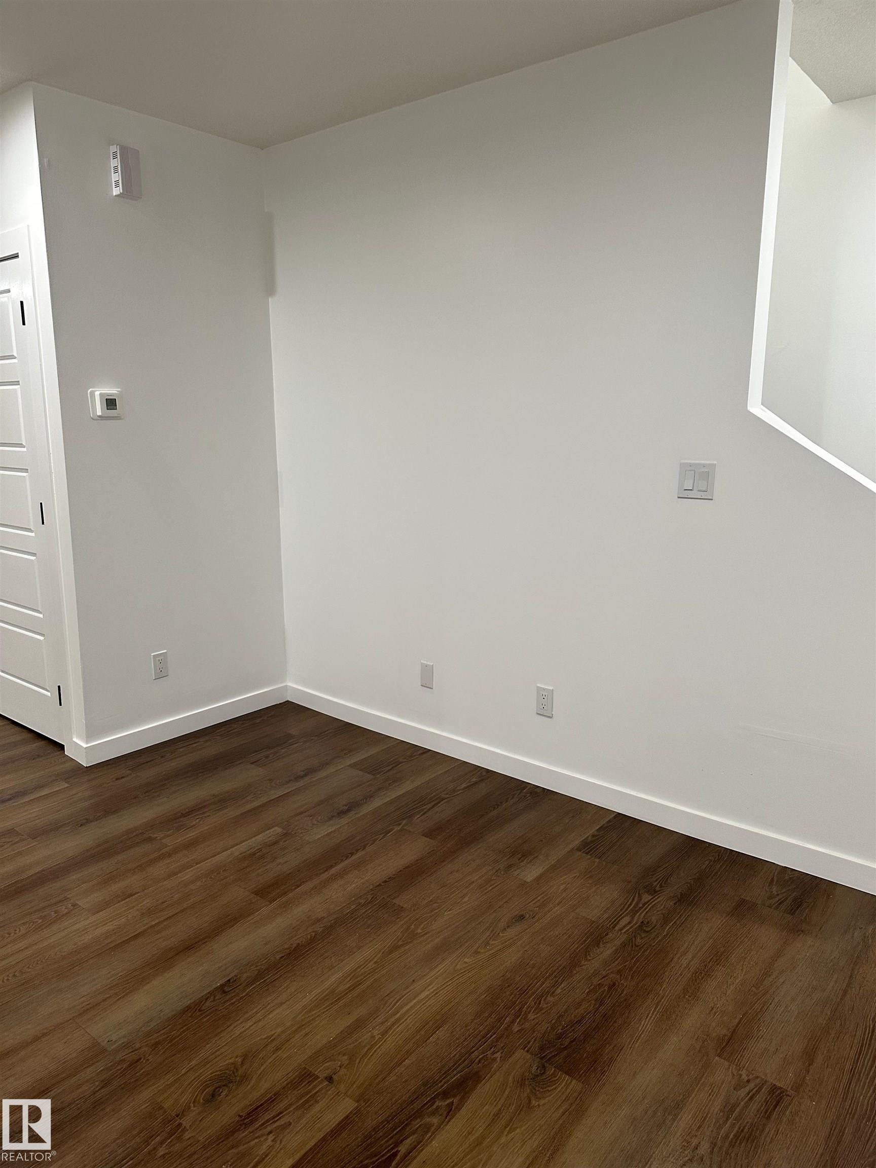 Wood-finish flooring with white baseboards and light-toned walls - 104 Meadowview Way, Leduc, AB - Indoor Photo Showing Other Room