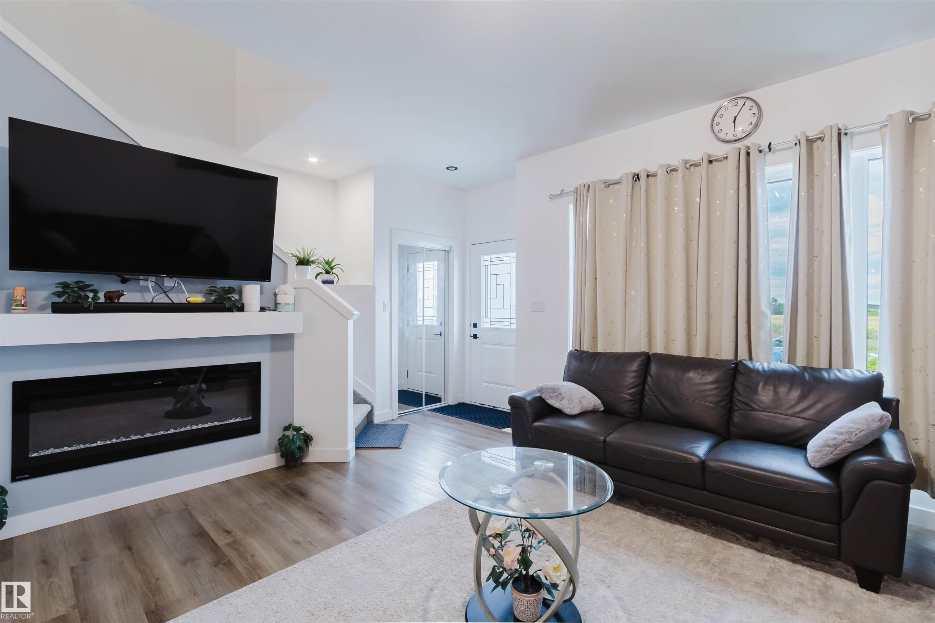 Living area featuring wood-finish flooring, a built-in electric fireplace, recessed lighting, and a white paneled door - 104 Meadowview Way, Leduc, AB - Indoor Photo Showing Living Room With Fireplace