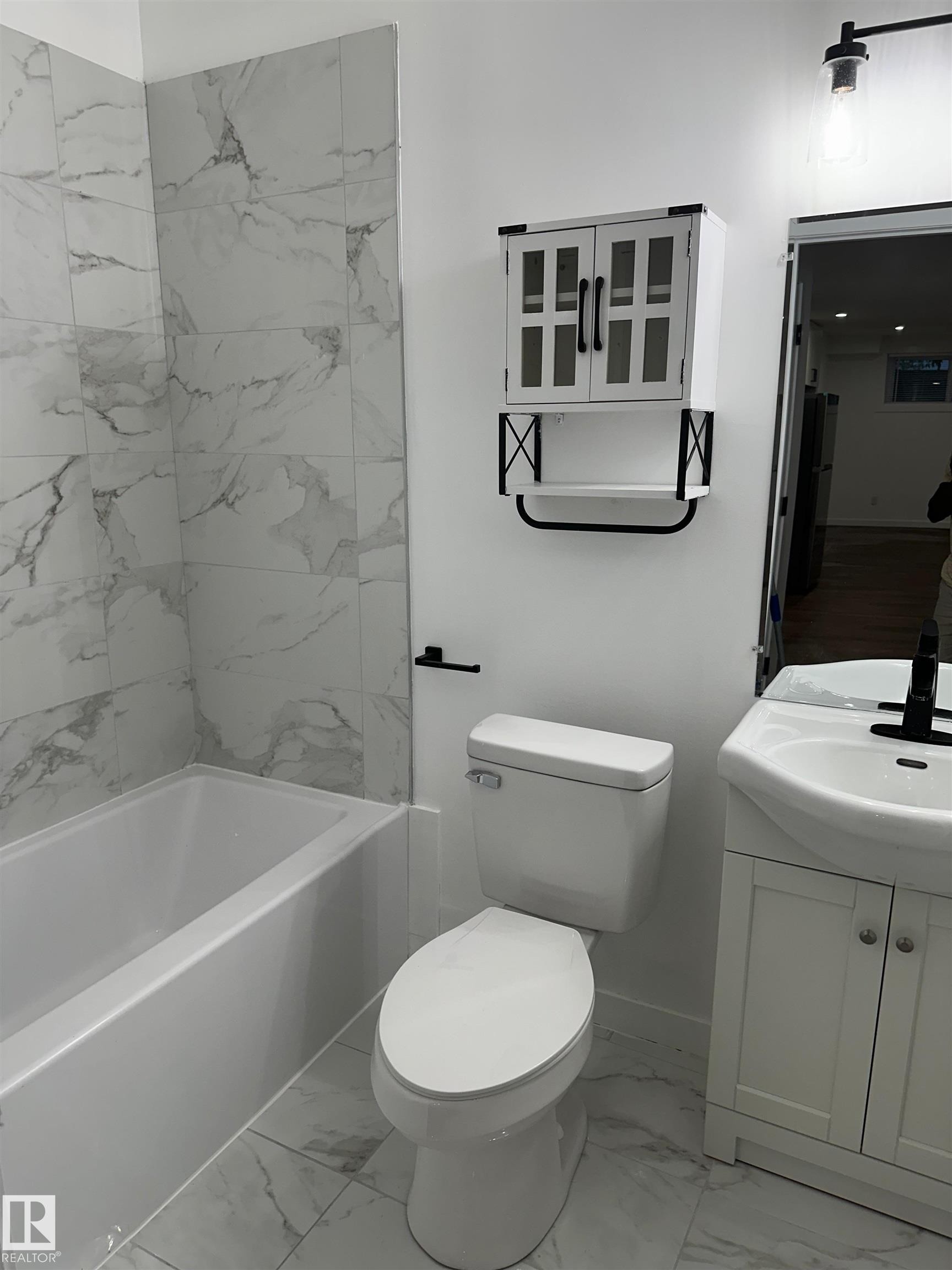 Bathroom featuring a white bathtub, wall-mounted cabinet with glass-front doors, white vanity with an integrated sink, and large format floor and wall tile - 104 Meadowview Way, Leduc, AB - Indoor Photo Showing Bathroom