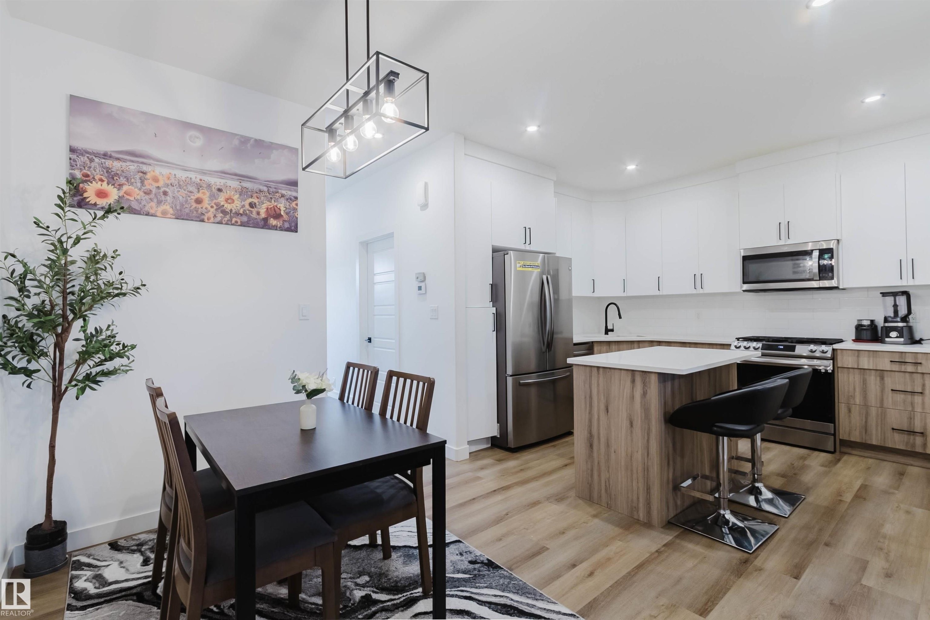 Contemporary kitchen featuring stainless steel appliances, a center island with countertop seating, white upper cabinetry, and wood-finish lower cabinetry - 104 Meadowview Way, Leduc, AB - Indoor