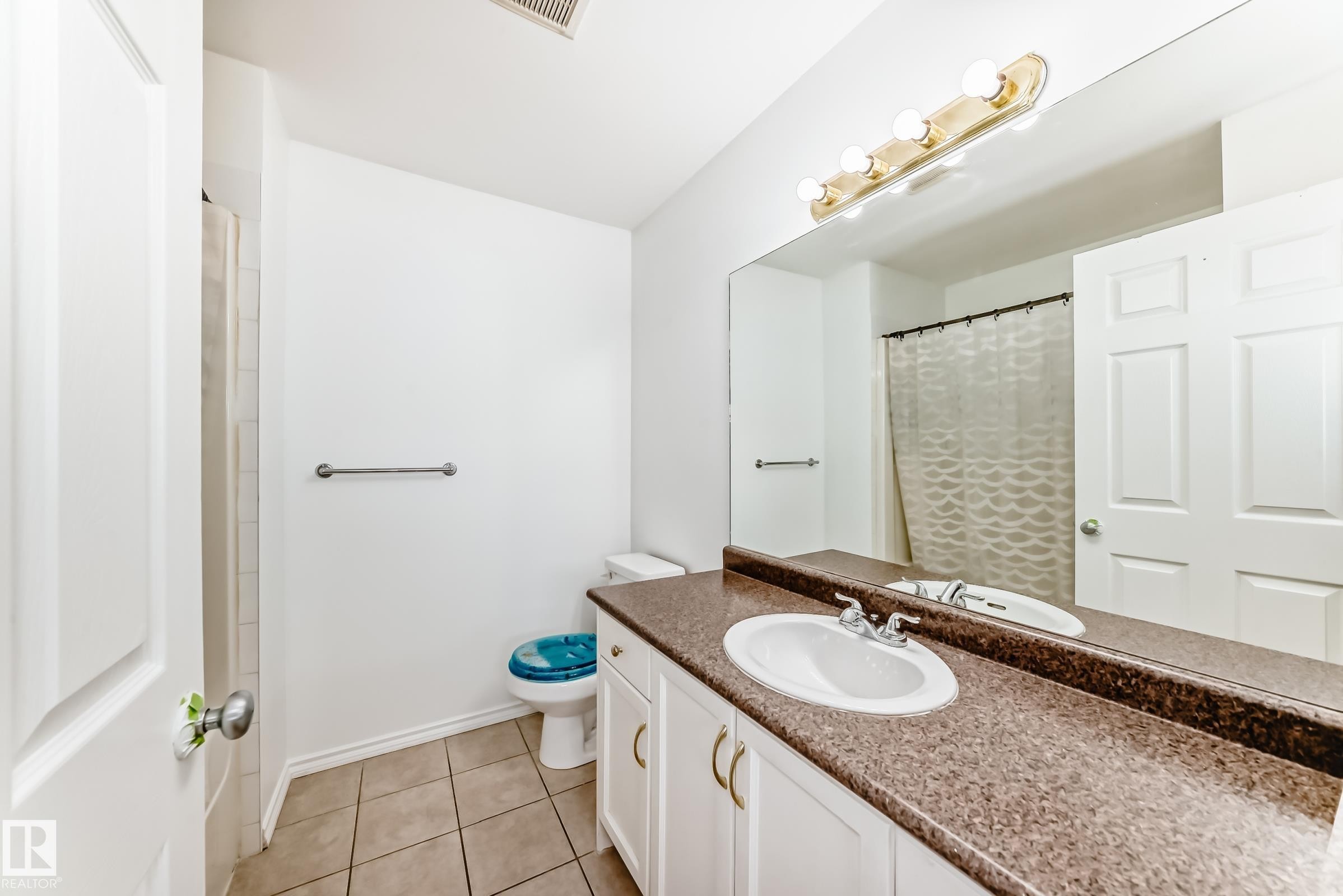 Vanity with a brown speckled countertop and an integrated sink, white cabinetry with gold-tone hardware, a full-width mirror, and a wall-mounted light fixture - 11727 83 Street Nw, Edmonton, AB - Indoor Photo Showing Bathroom