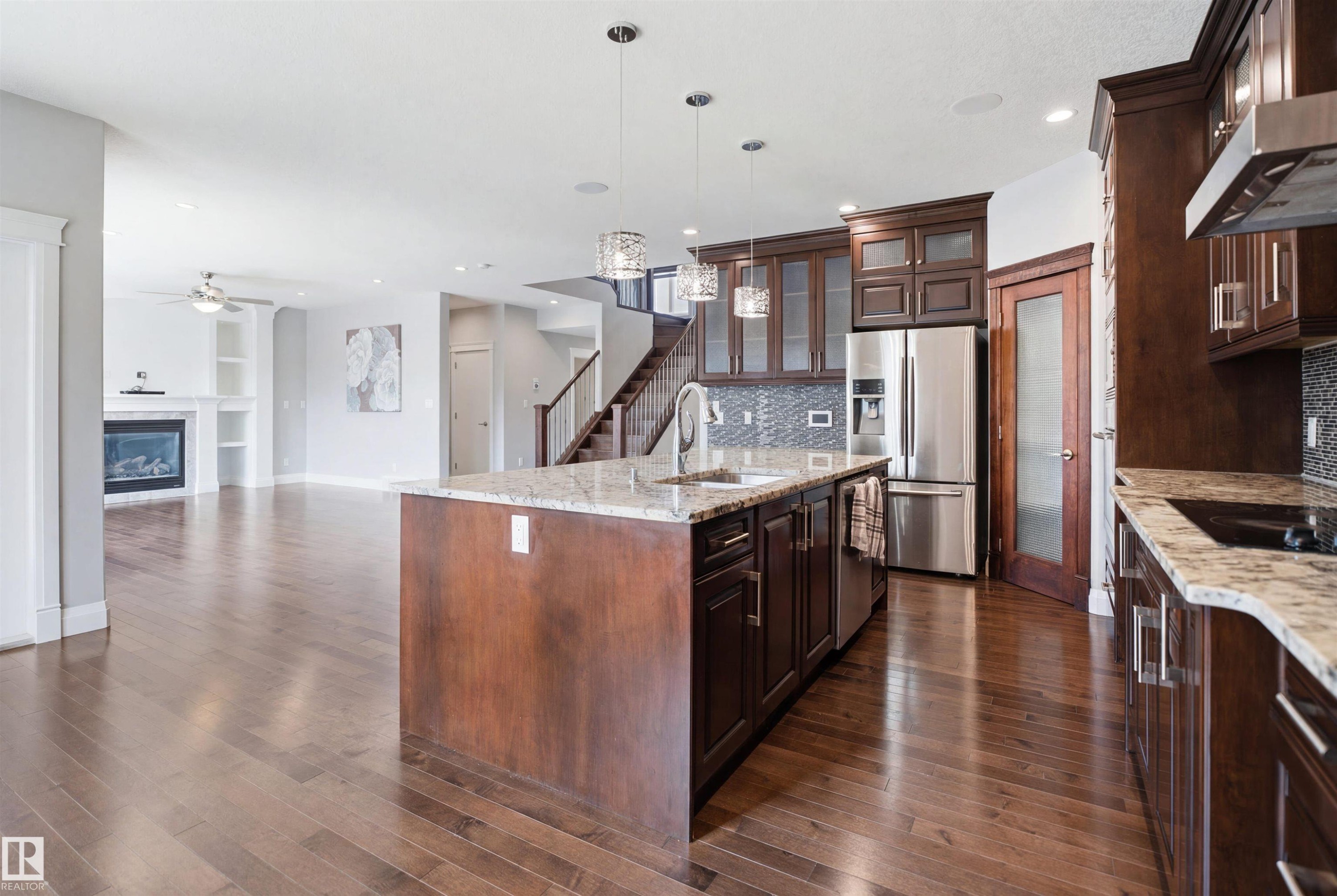 Hardwood flooring throughout, kitchen island with built-in sink, stainless steel appliances, dark wood-finish cabinetry, and a fireplace with built-in shelving - 427 Windermere Road Nw, Edmonton, AB - Indoor Photo Showing Kitchen With Upgraded Kitchen