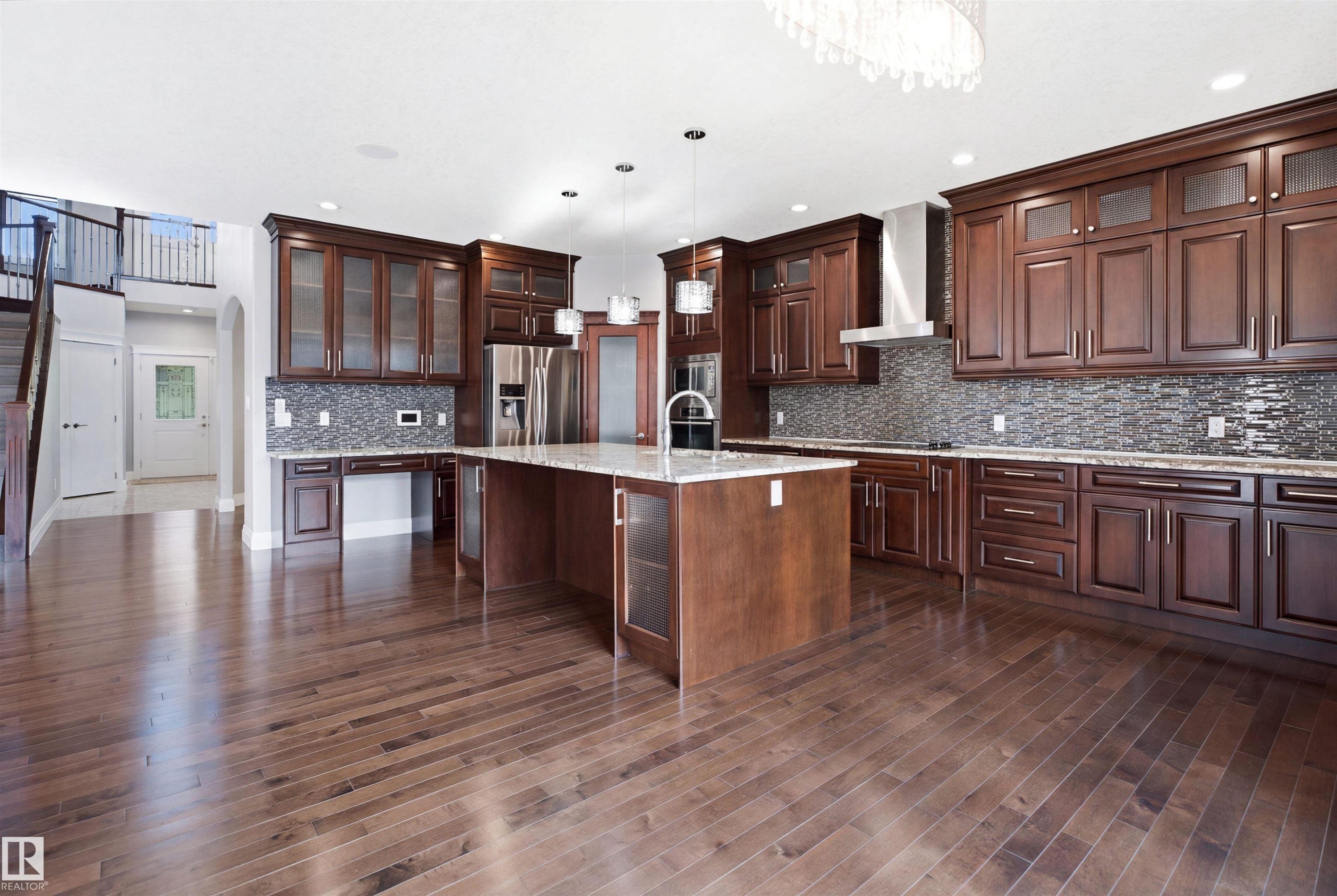 Wood-finish flooring throughout, kitchen island with built-in sink, stainless steel appliances, dark wood cabinetry, and mosaic tile backsplash - 427 Windermere Road Nw, Edmonton, AB - Indoor Photo Showing Kitchen With Upgraded Kitchen