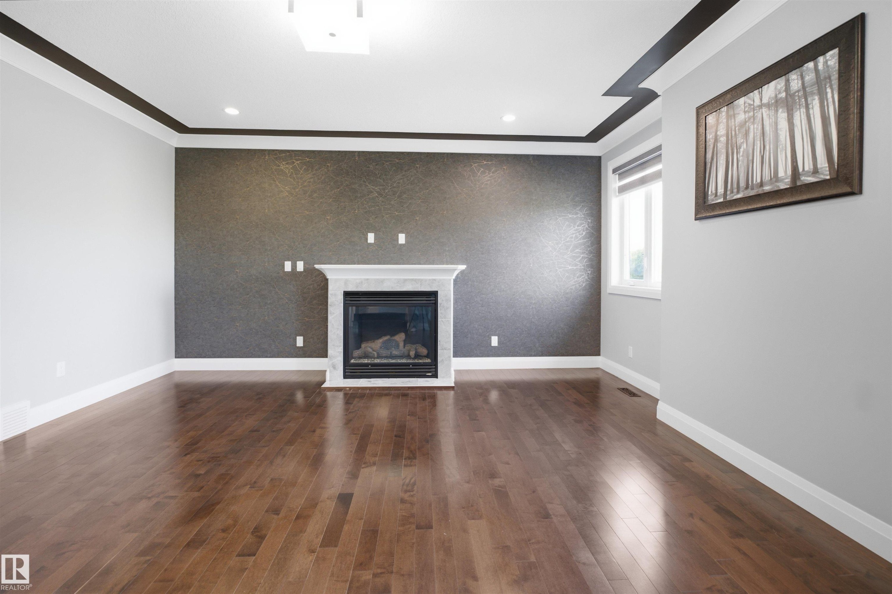 Hardwood flooring, fireplace with a marble-style surround, accent wall, crown molding, and a window with a roller shade - 427 Windermere Road Nw, Edmonton, AB - Indoor With Fireplace