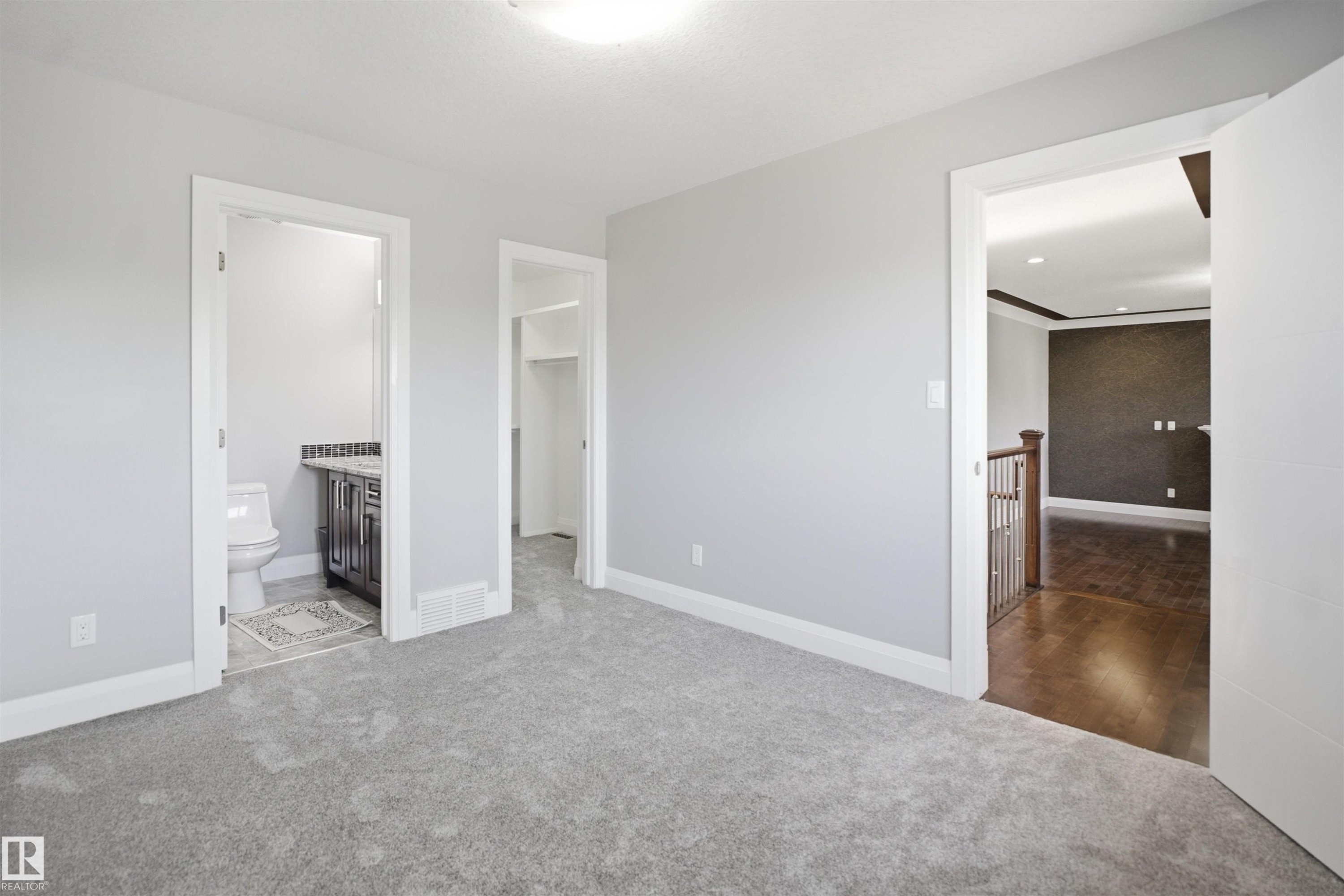 Carpeted room with light gray walls, an attached bathroom featuring a dark vanity with a light countertop, and an adjacent closet space - 427 Windermere Road Nw, Edmonton, AB - Indoor