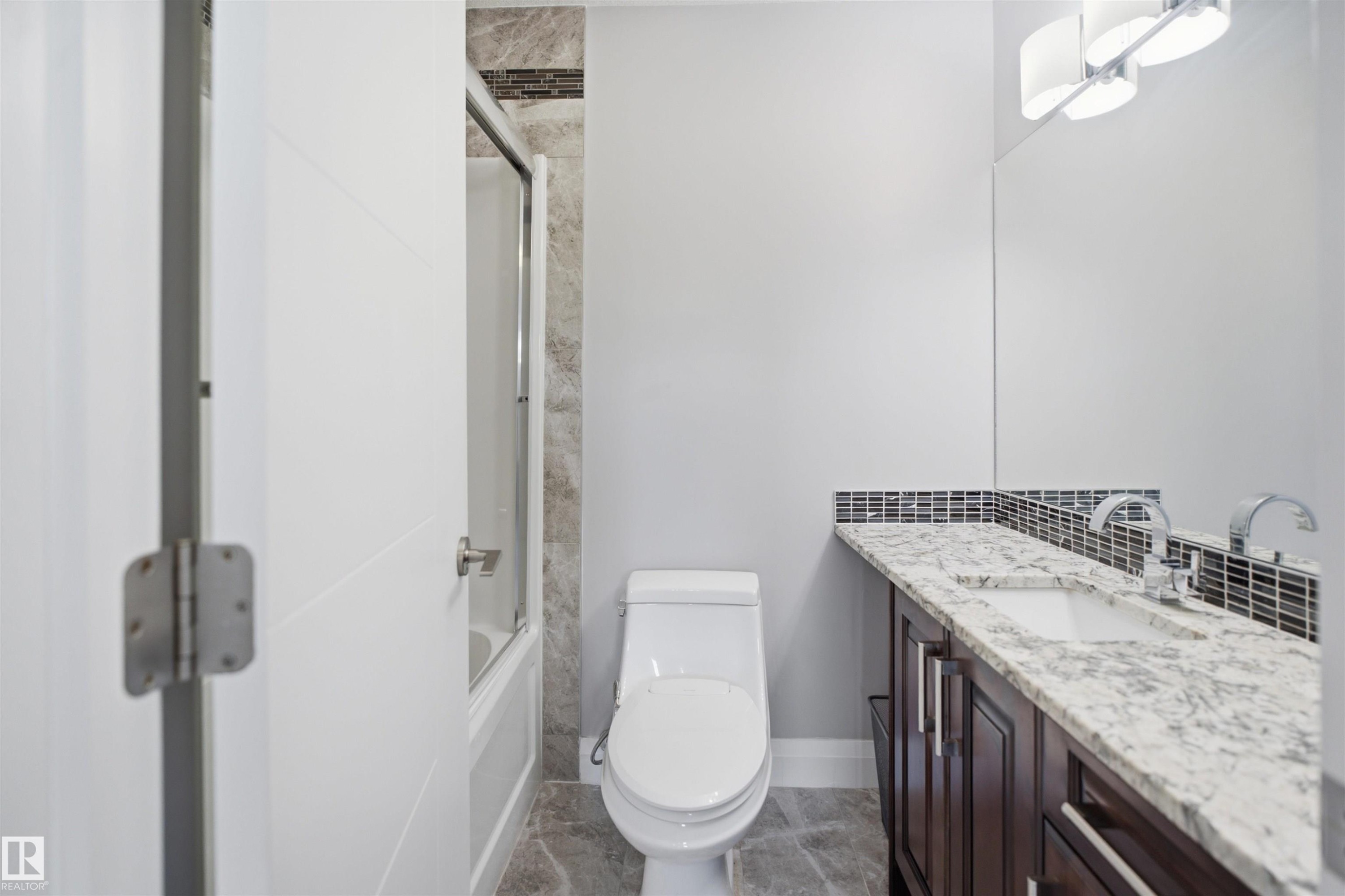 White flat panel door, full-size built-in bathtub with glass enclosure, white toilet, dark wood-finish vanity with drawer and cabinet storage, and a white countertop with an undermount sink - 427 Windermere Road Nw, Edmonton, AB - Indoor Photo Showing Bathroom