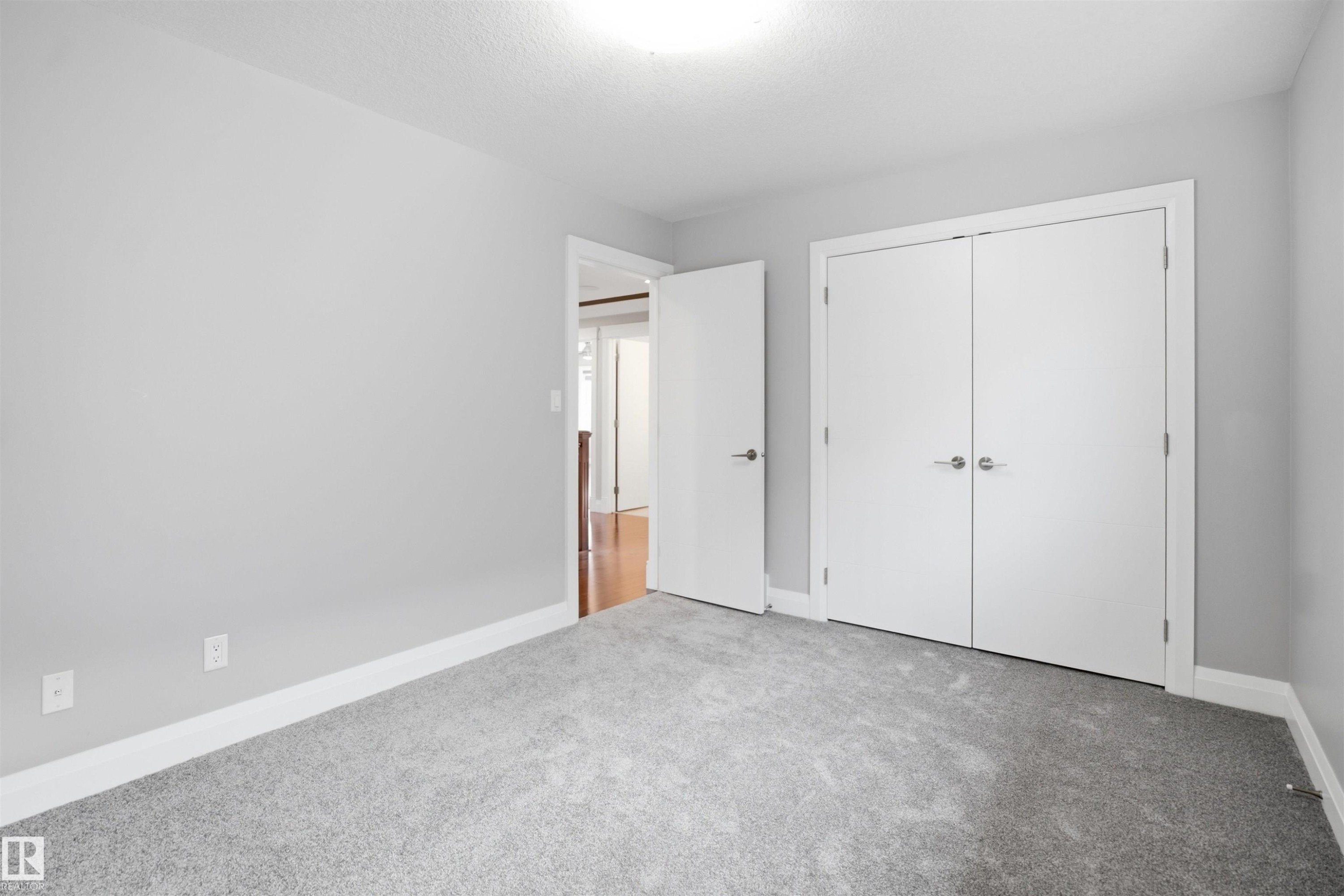 Gray wall paint with white trim, gray carpet flooring, white bi-fold closet doors, and white interior doors with satin nickel hardware - 427 Windermere Road Nw, Edmonton, AB - Indoor Photo Showing Other Room