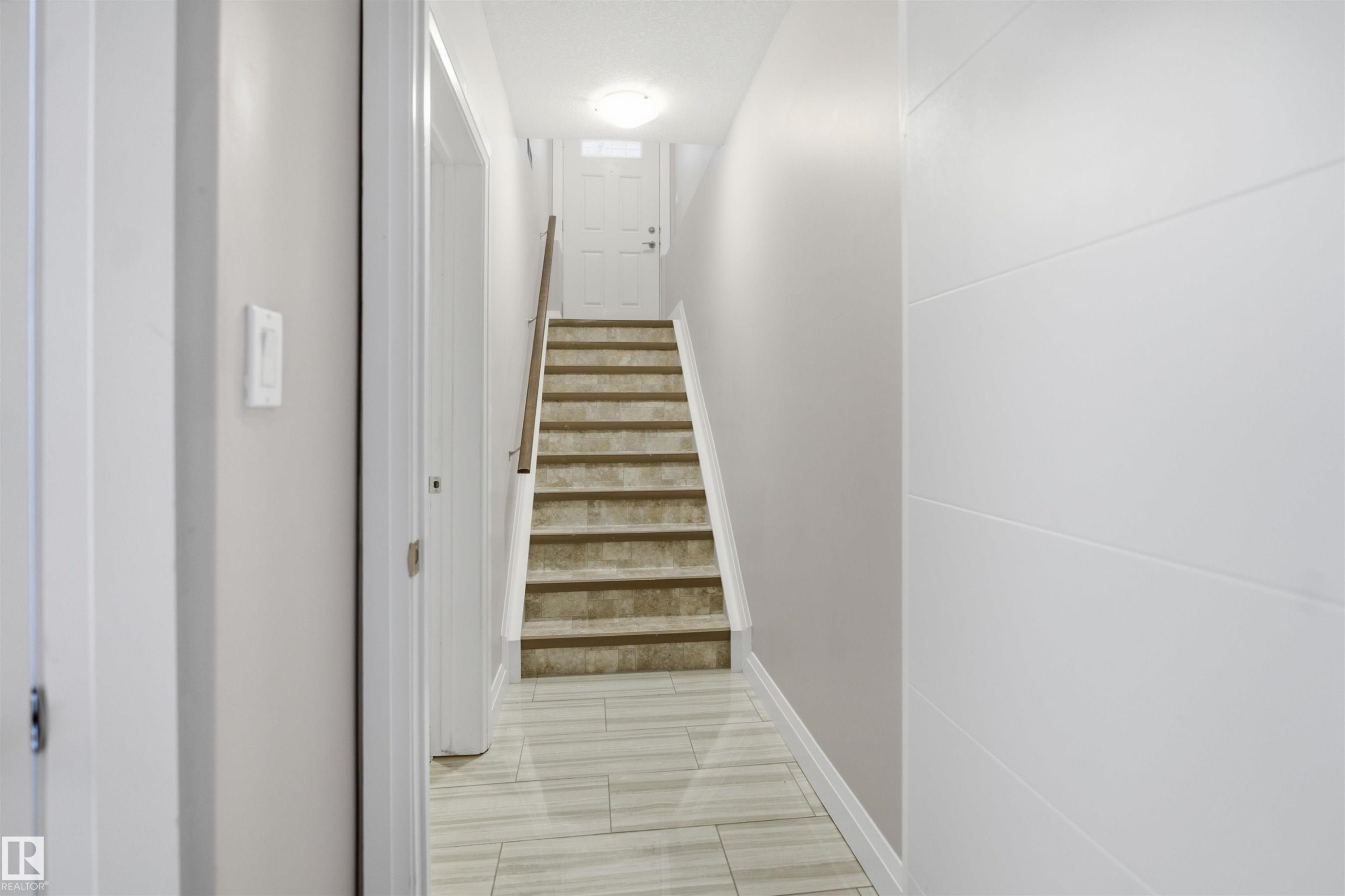 Tiled flooring leading to carpeted stairs with a wood handrail - 427 Windermere Road Nw, Edmonton, AB - Indoor Photo Showing Other Room