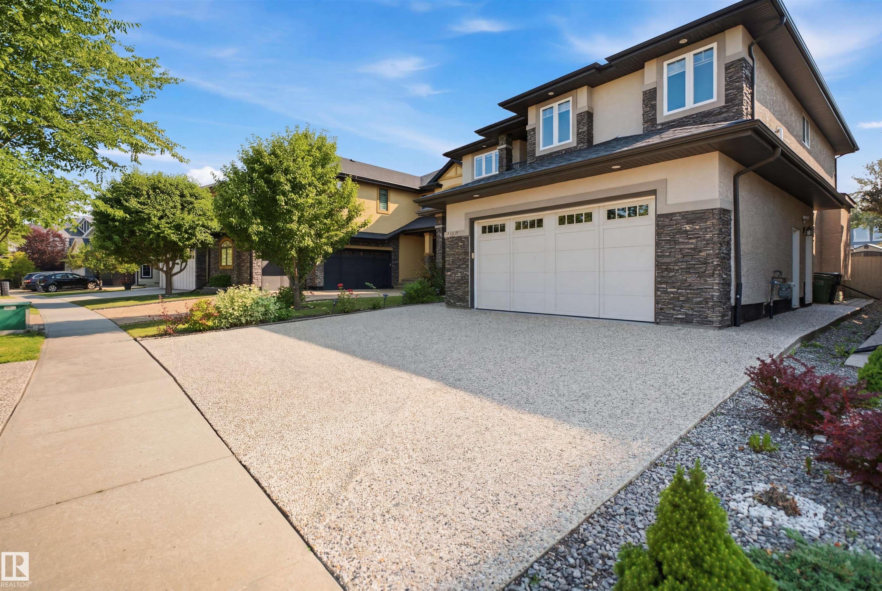 Two-story stucco and stone exterior featuring a two-car garage and a gravel driveway - 427 Windermere Road Nw, Edmonton, AB - Outdoor