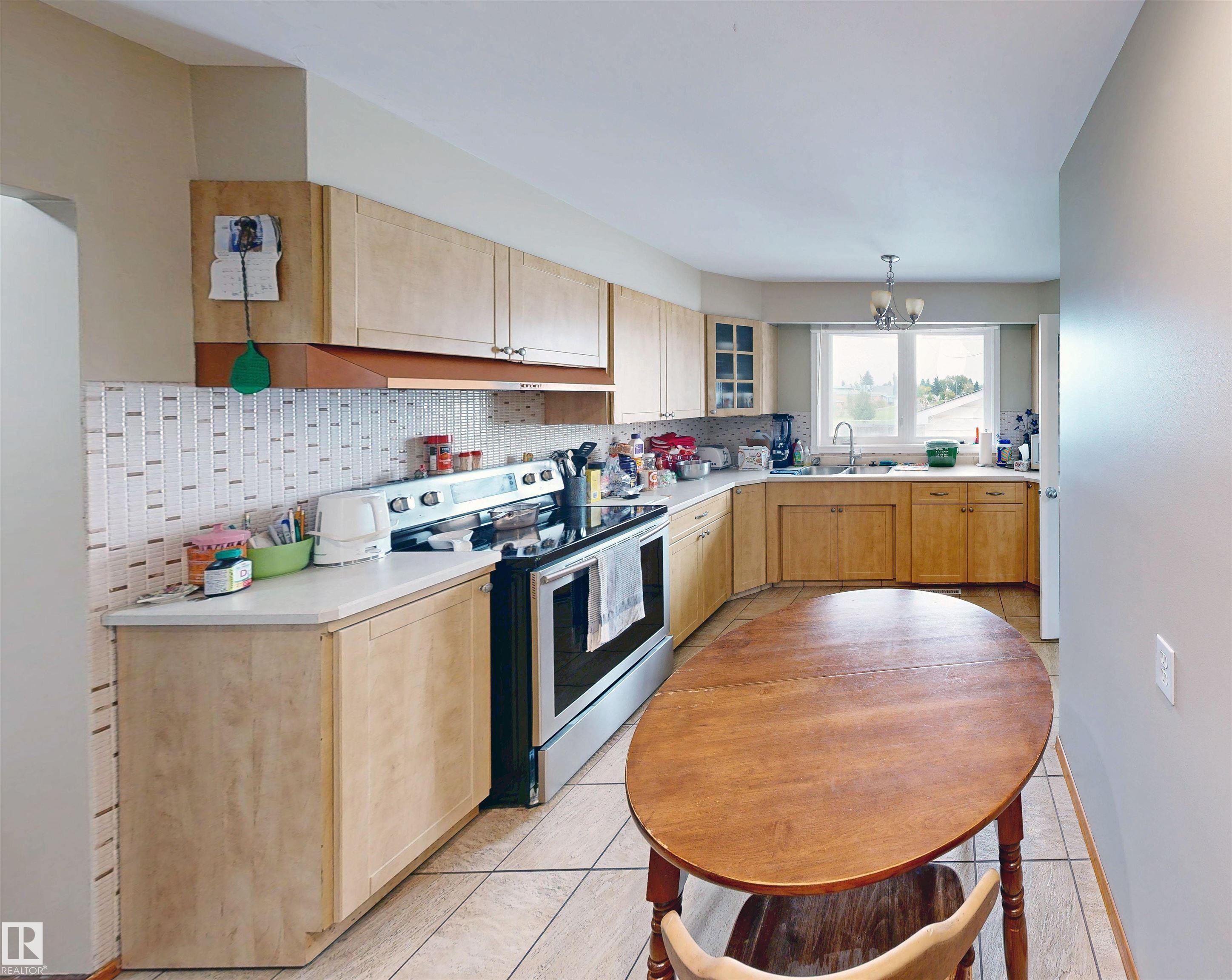 Kitchen featuring wood-finish cabinetry, white countertops, a mosaic tile backsplash, and stainless steel appliances - 9531 74 Street Nw, Edmonton, AB - Indoor Photo Showing Kitchen With Double Sink