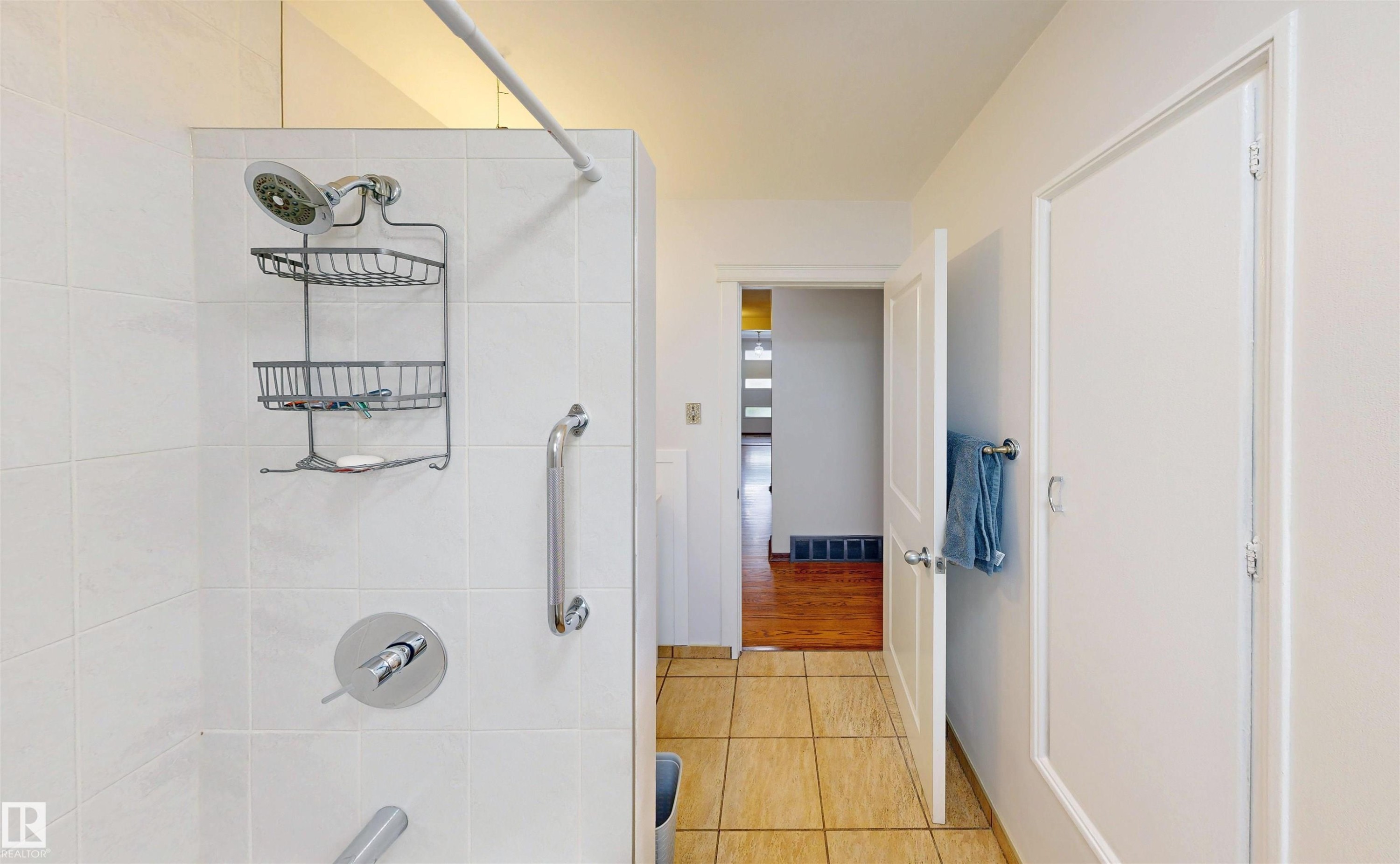 White tiled shower with a chrome showerhead and grab bar - 9531 74 Street Nw, Edmonton, AB - Indoor Photo Showing Bathroom