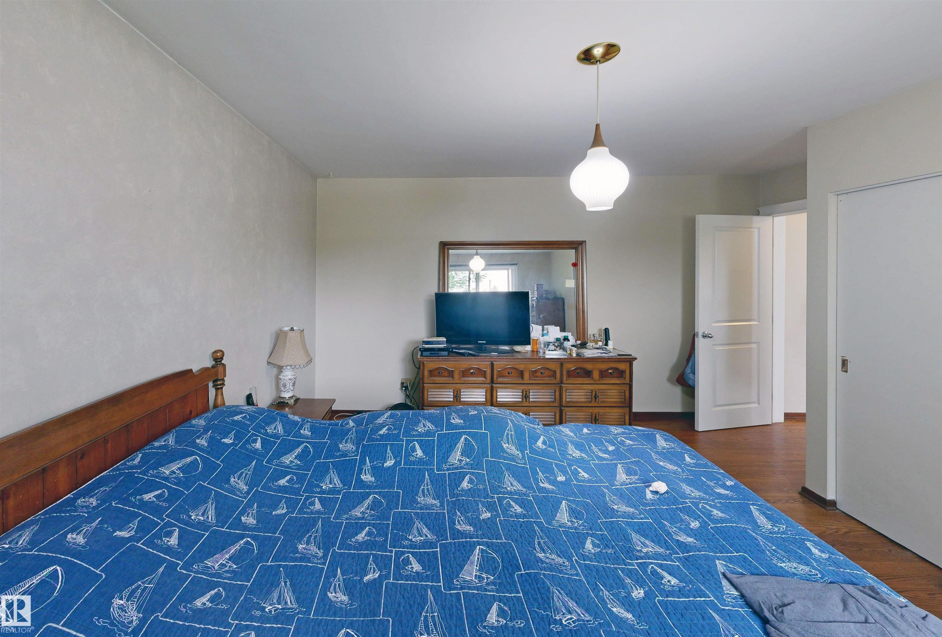 Wood-finish flooring, two-panel interior doors, and a contemporary pendant light fixture - 9531 74 Street Nw, Edmonton, AB - Indoor Photo Showing Bedroom