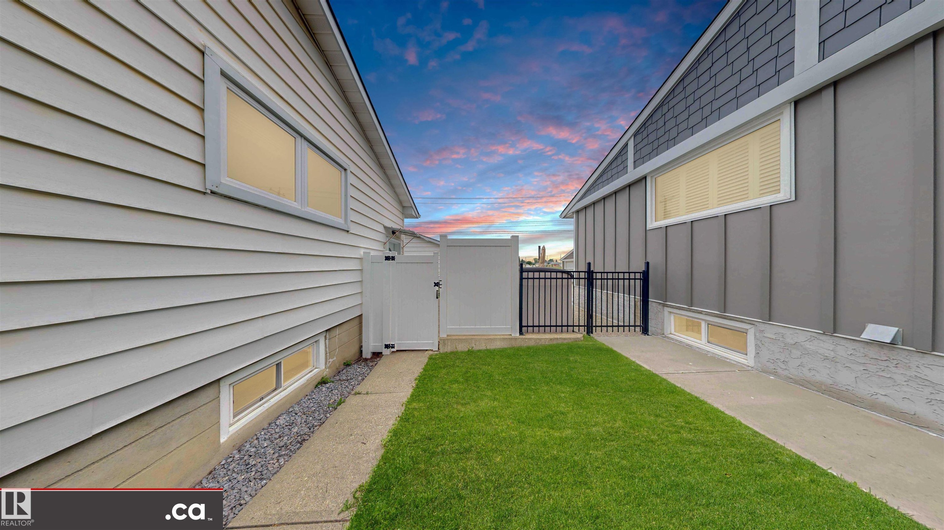 Manicured lawn, concrete pathway, white vinyl fencing, black metal gate, and exterior siding - 9531 74 Street Nw, Edmonton, AB - Outdoor With Exterior