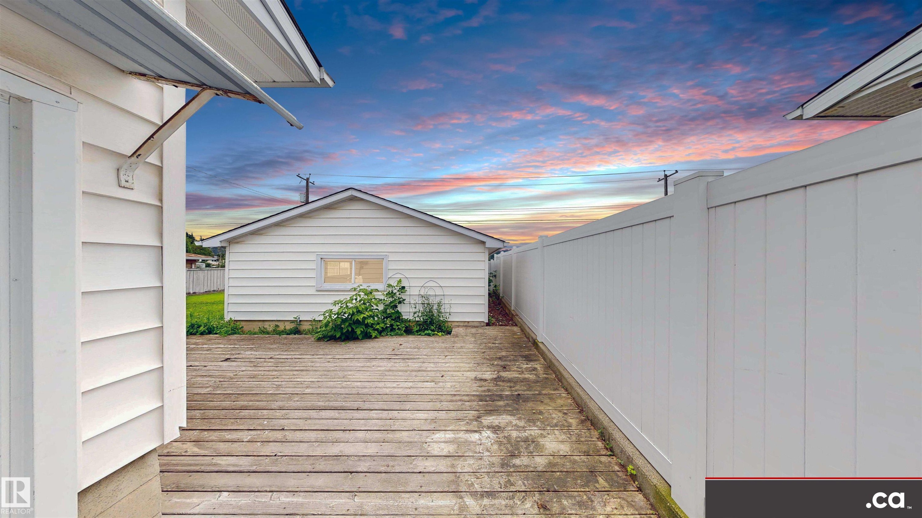 Wood-finish deck with a detached white-sided structure and white panel fencing - 9531 74 Street Nw, Edmonton, AB - Outdoor With Exterior