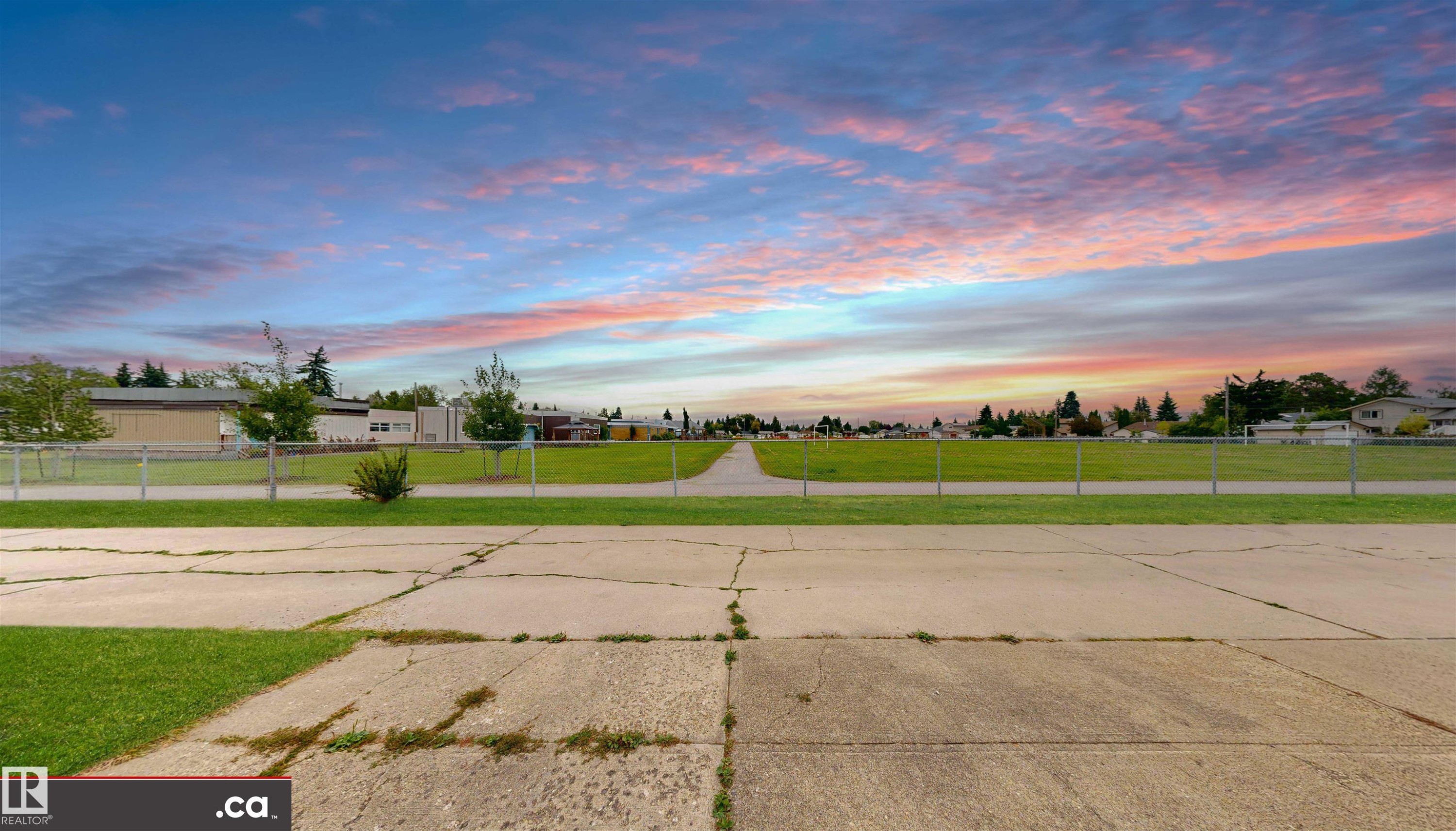 Expansive green space bordered by a chain-link fence, with buildings and mature trees in the background - 9531 74 Street Nw, Edmonton, AB - Outdoor With View