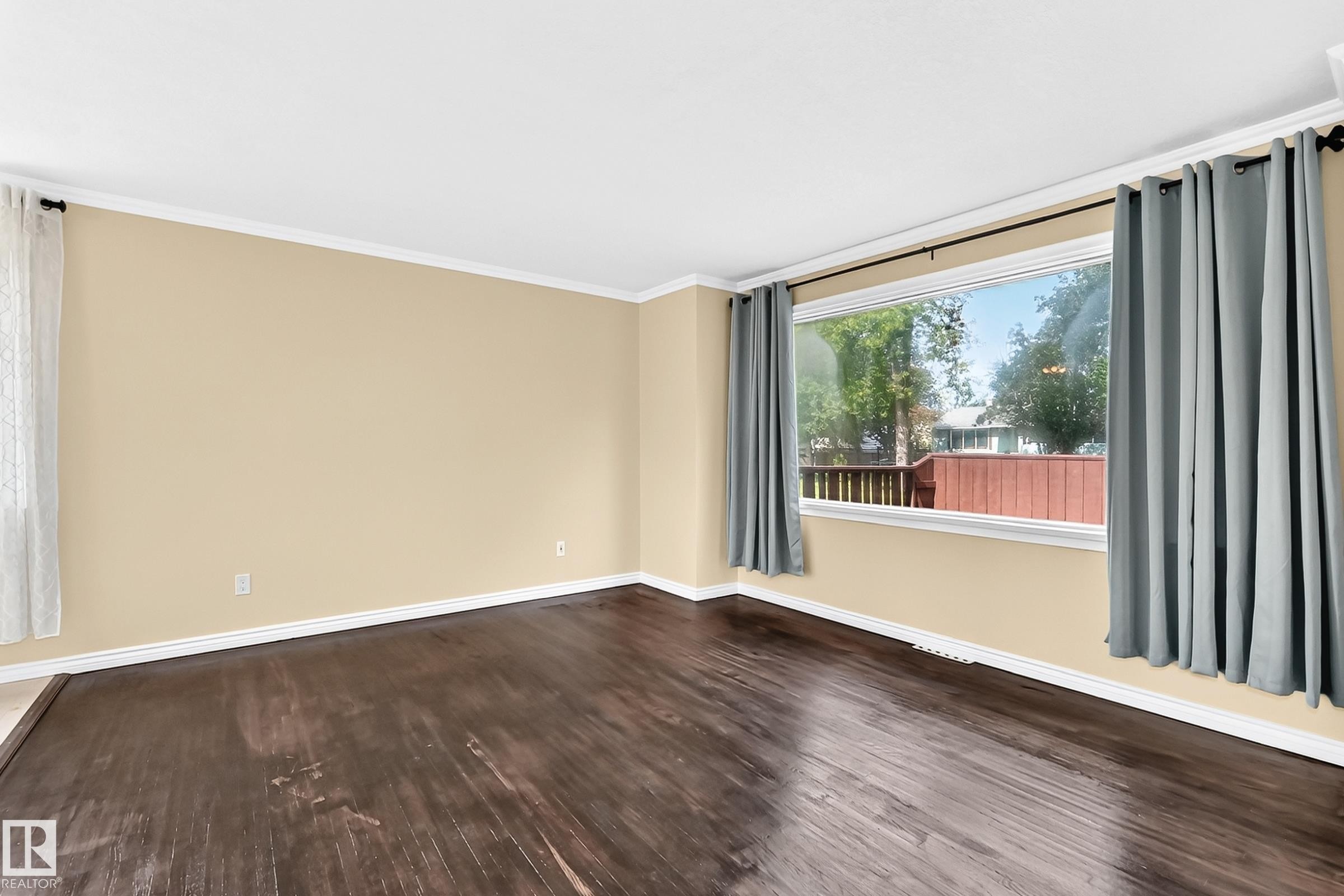 Wood-finish flooring, crown molding, and a large window with white trim - 50 Rocque, Fort Saskatchewan, AB - Indoor Photo Showing Other Room