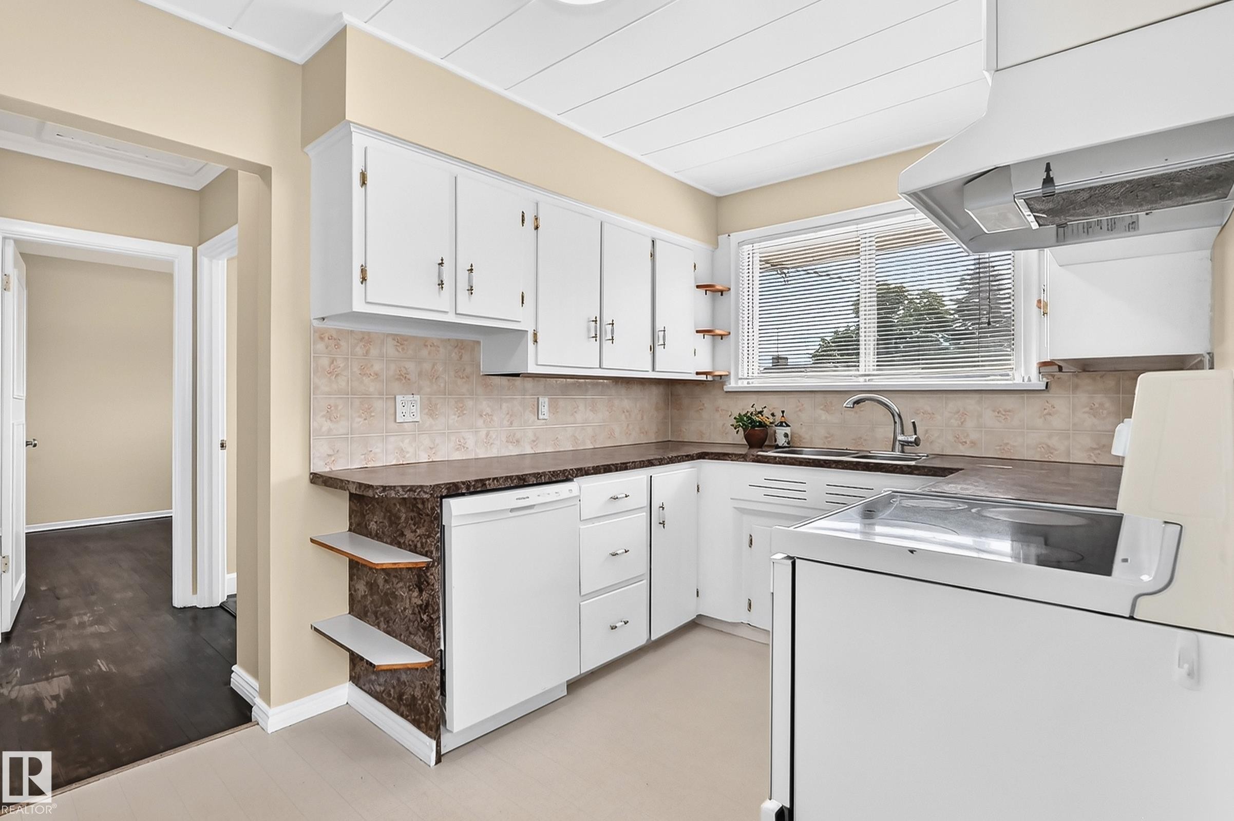 Kitchen featuring white cabinetry, a stainless-steel sink with an attached faucet, a tiled backsplash, and dark-toned countertops - 50 Rocque, Fort Saskatchewan, AB - Indoor Photo Showing Kitchen