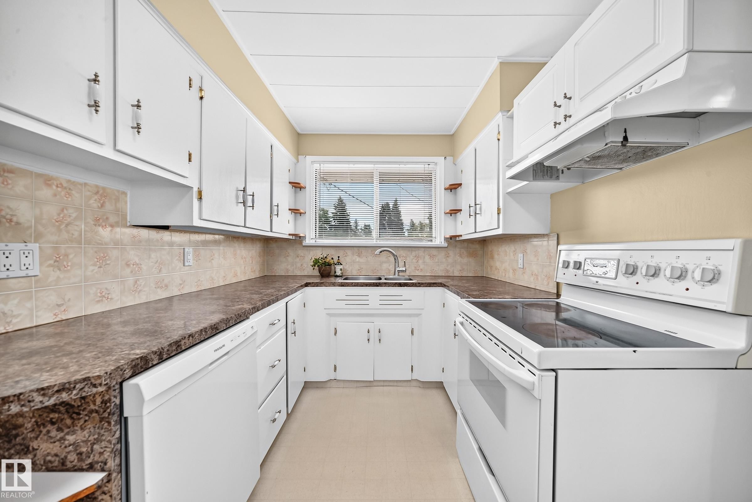 U-shaped kitchen featuring white cabinetry, a built-in dishwasher, an electric range, a stainless steel sink, and patterned backsplash tiling - 50 Rocque, Fort Saskatchewan, AB - Indoor Photo Showing Kitchen With Double Sink