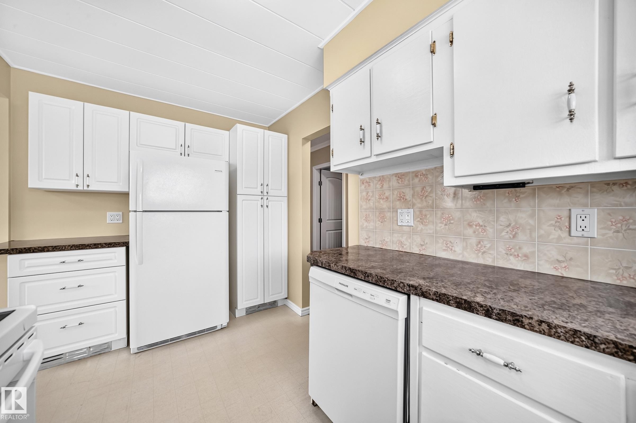 White cabinetry, patterned tile backsplash, dark countertops, built-in dishwasher, and recessed lighting - 50 Rocque, Fort Saskatchewan, AB - Indoor Photo Showing Kitchen