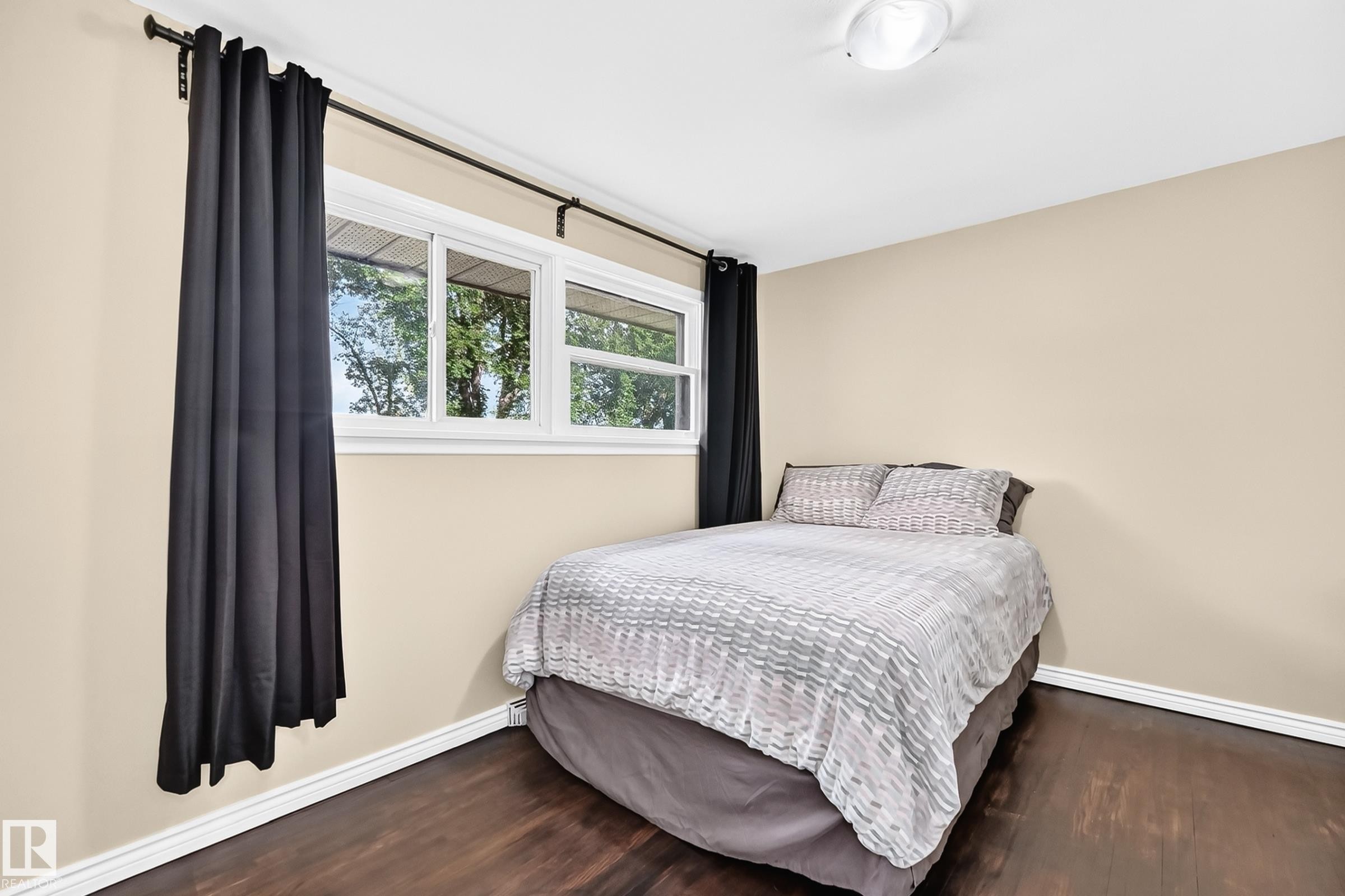 Wood-finish flooring with white trim, neutral wall color, and a multi-pane window - 50 Rocque, Fort Saskatchewan, AB - Indoor Photo Showing Bedroom