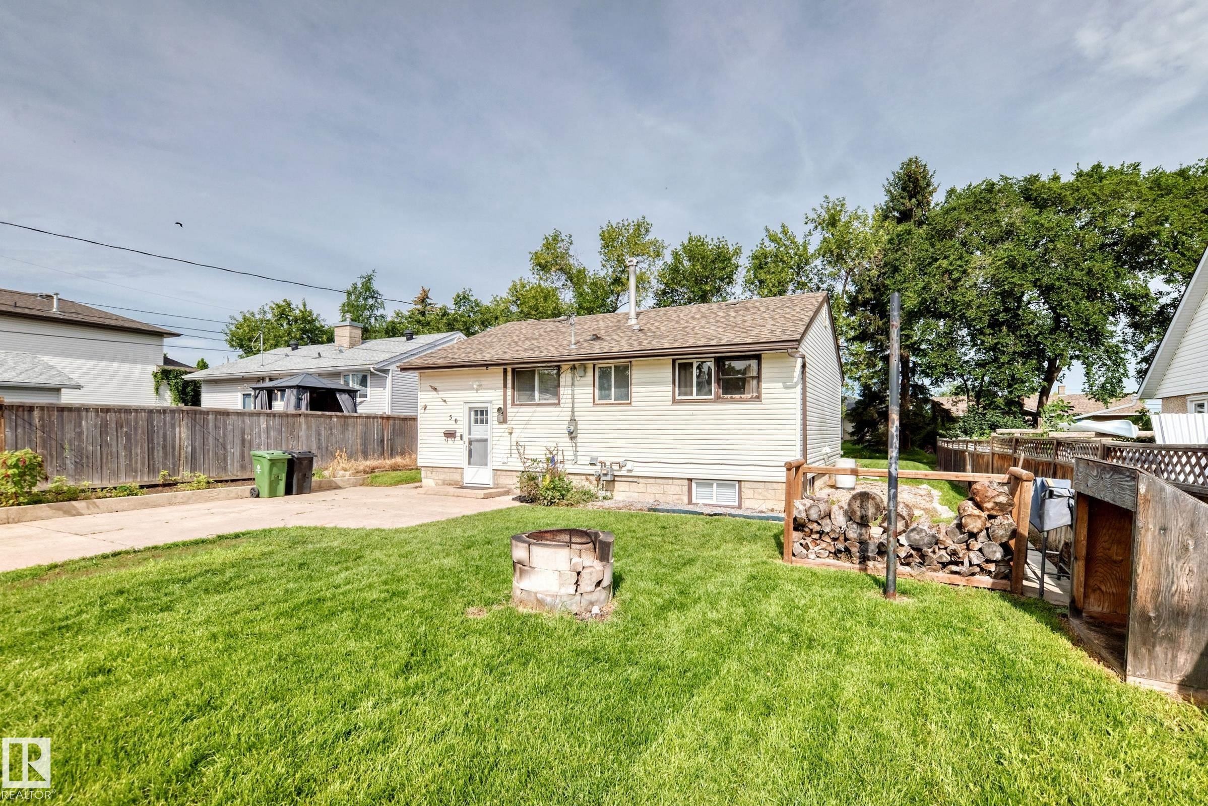 Expansive backyard featuring a manicured lawn, concrete patio, and a wood privacy fence - 50 Rocque, Fort Saskatchewan, AB - Outdoor
