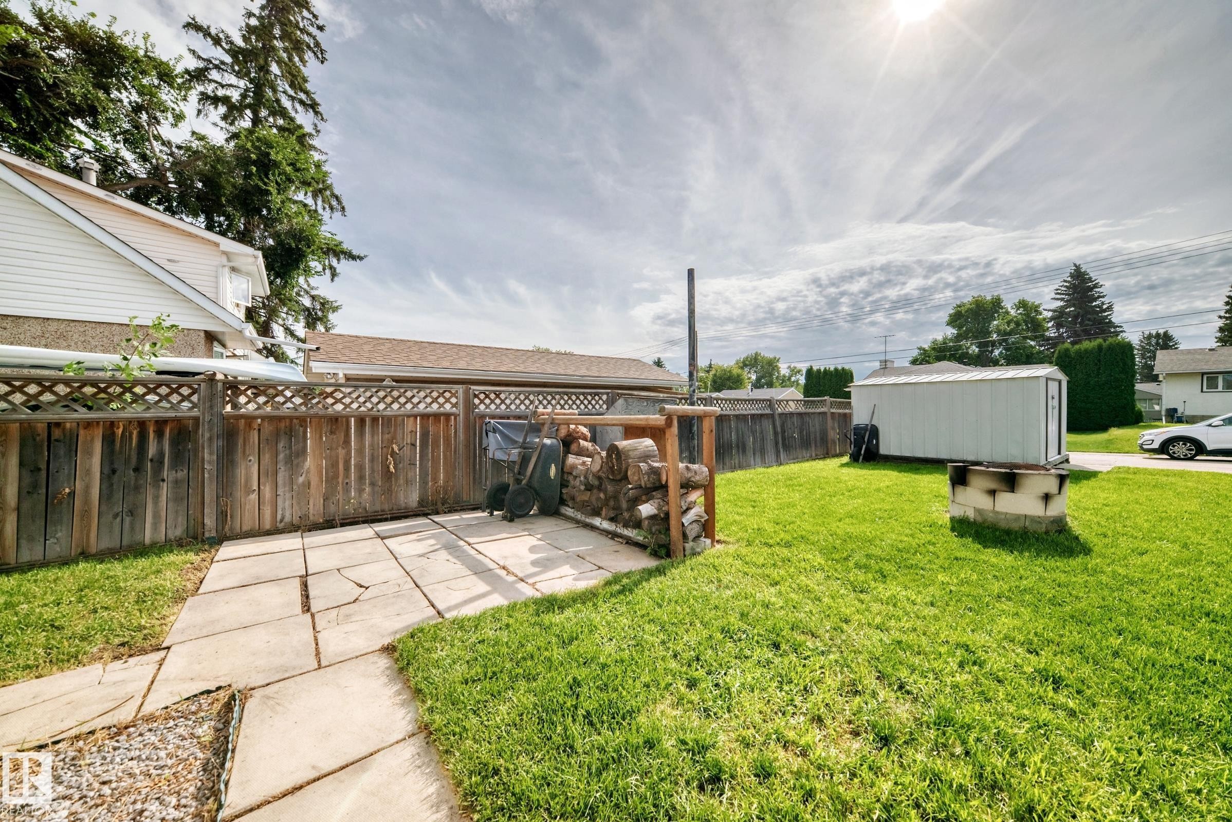 Expansive backyard featuring a stone patio, vibrant green lawn, wood privacy fencing, and an on-site storage shed - 50 Rocque, Fort Saskatchewan, AB - Outdoor