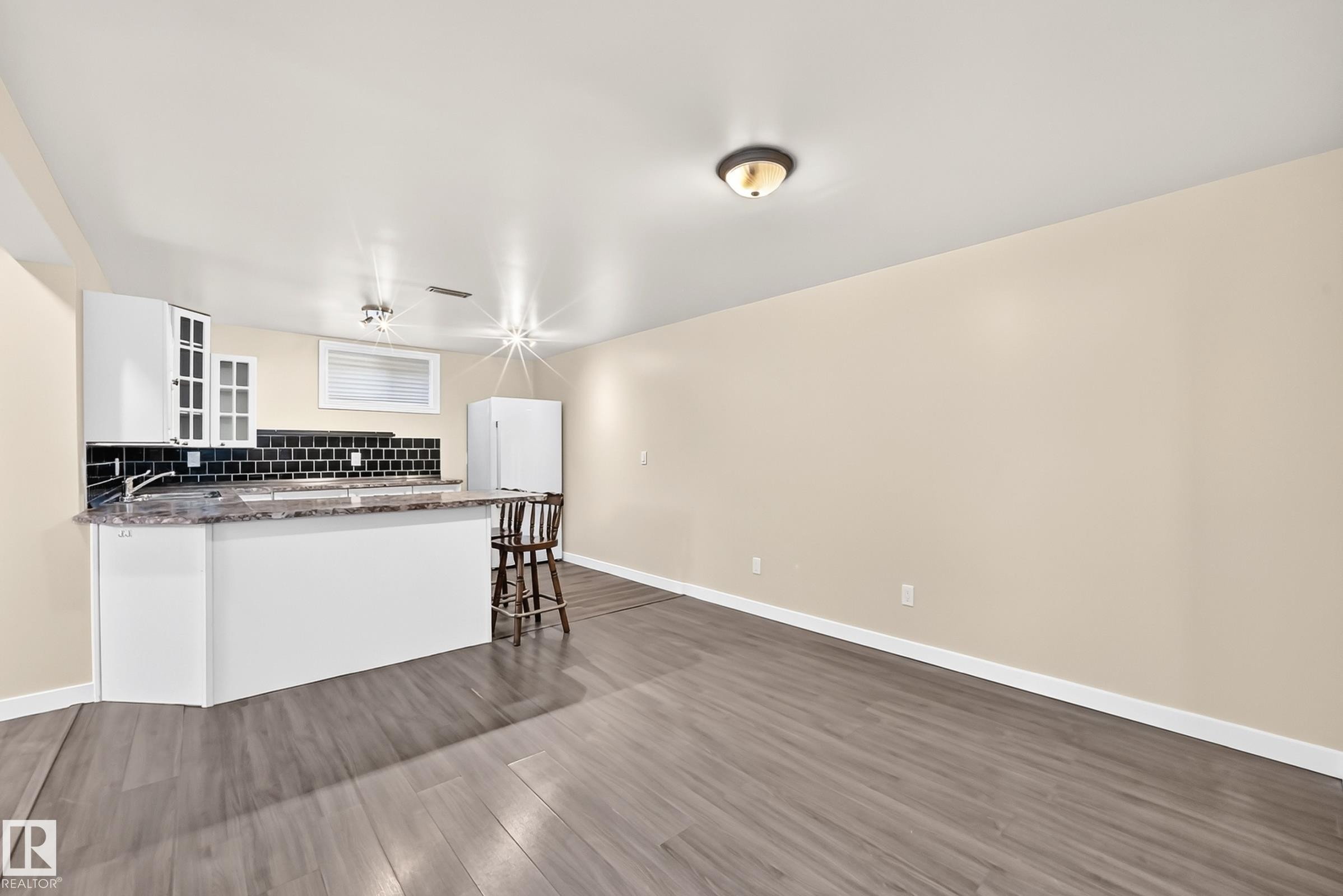 Kitchenette with white cabinetry, black subway tile backsplash, and a breakfast bar with a stone-finish countertop - 50 Rocque, Fort Saskatchewan, AB - Indoor Photo Showing Kitchen