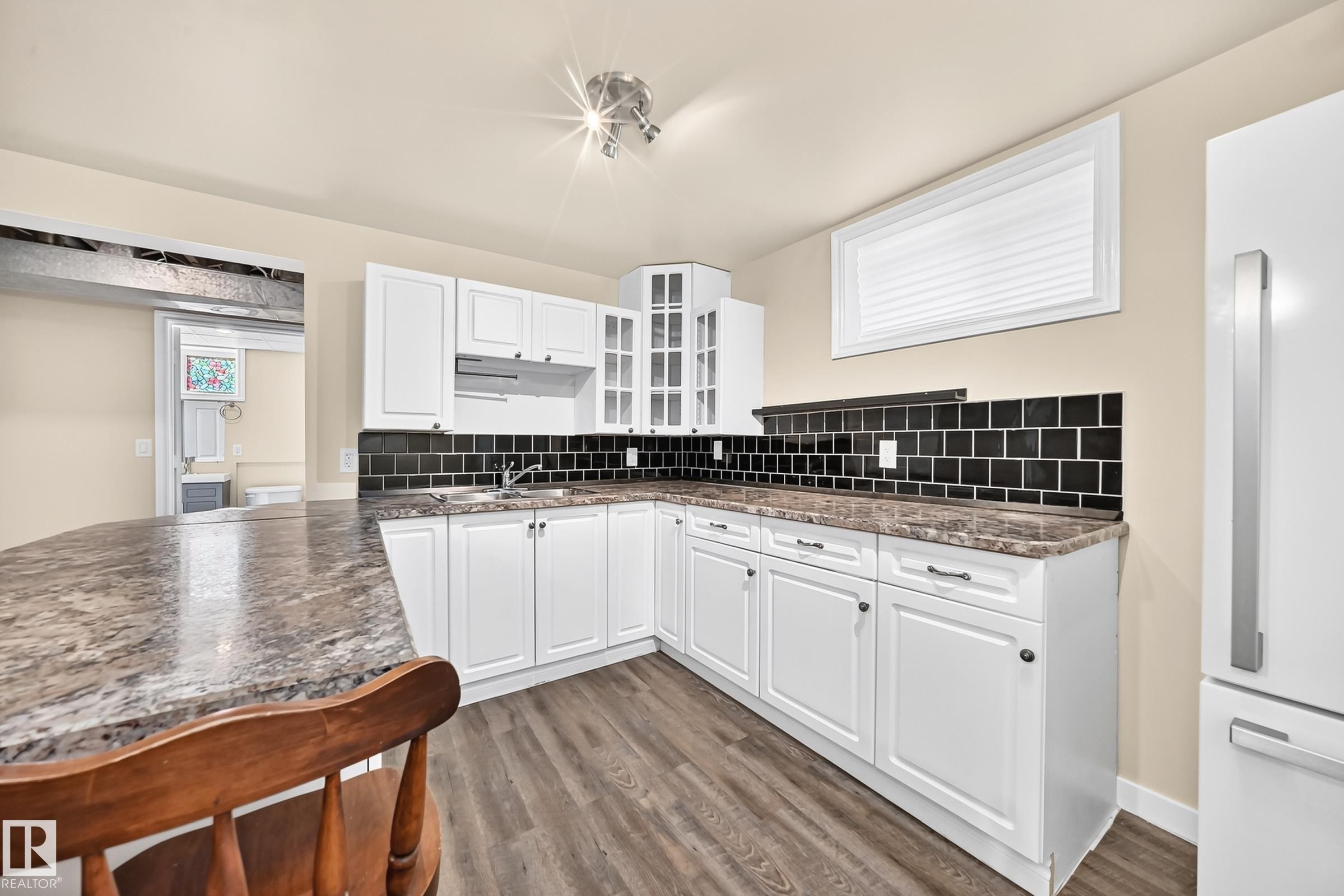 White cabinetry with dark hardware, dark tiled backsplash, wood-finish flooring, and a stone-finish countertop - 50 Rocque, Fort Saskatchewan, AB - Indoor Photo Showing Kitchen