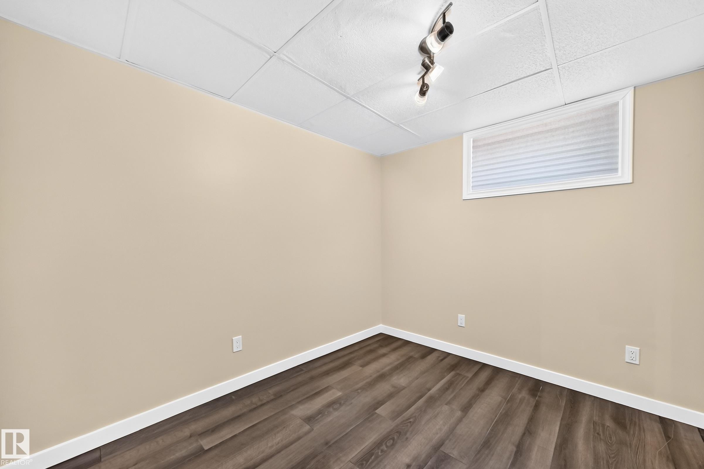 Wood-finish flooring with white baseboards, light-toned walls, and a drop ceiling with track lighting - 50 Rocque, Fort Saskatchewan, AB - Indoor Photo Showing Other Room