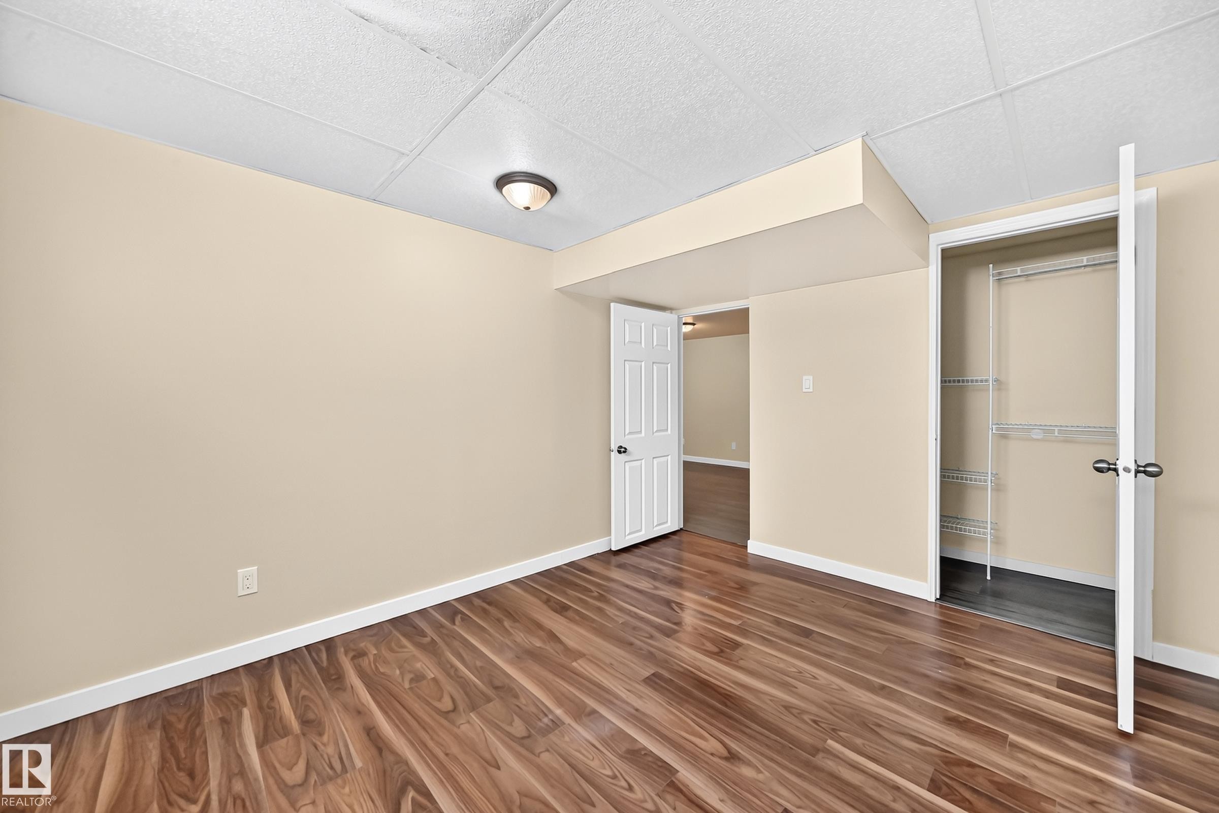 Wood-finish flooring, neutral wall tones, white trim, and a ceiling-mounted light fixture - 50 Rocque, Fort Saskatchewan, AB - Indoor Photo Showing Other Room