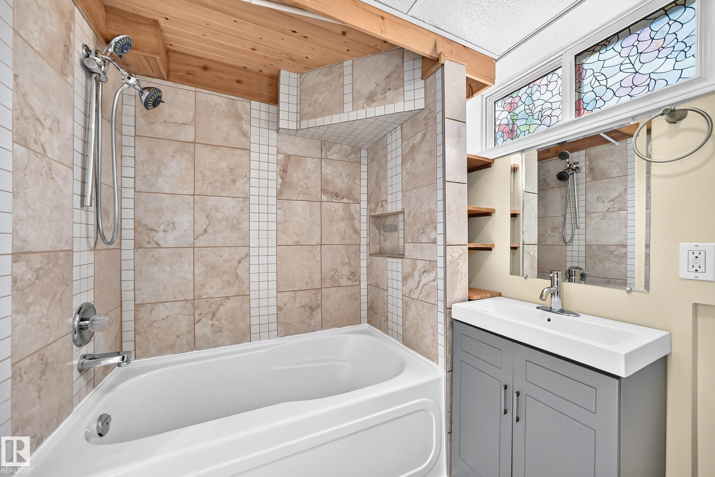 Bathroom featuring a built-in bathtub with shower, tiled surround, wood-finish ceiling, a vanity with an integrated sink, and an overhead transom window - 50 Rocque, Fort Saskatchewan, AB - Indoor Photo Showing Bathroom