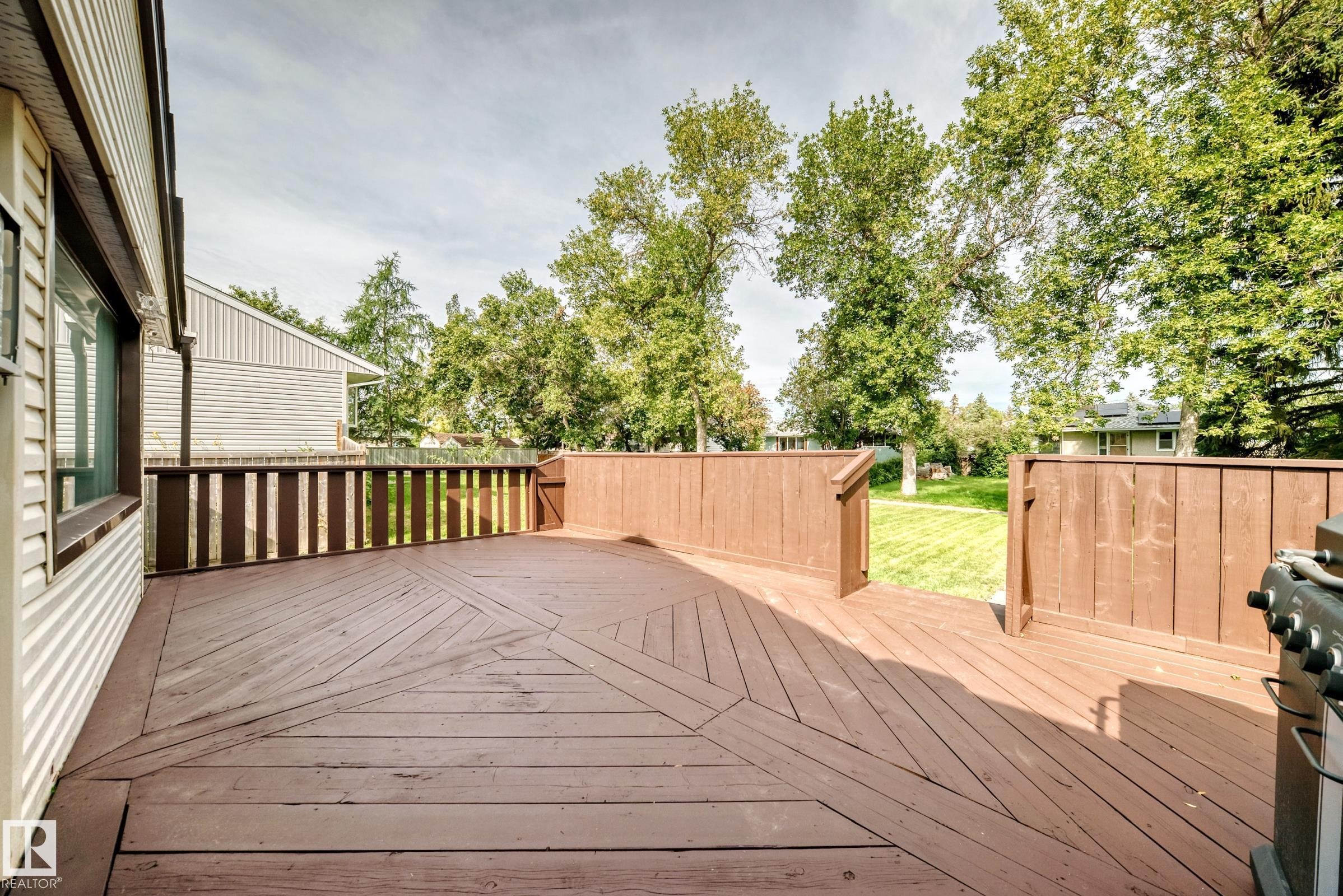 Expansive wood deck with a patterned floor design, wood railing, and direct access to a grassy yard - 50 Rocque, Fort Saskatchewan, AB - Outdoor With Deck Patio Veranda With Exterior