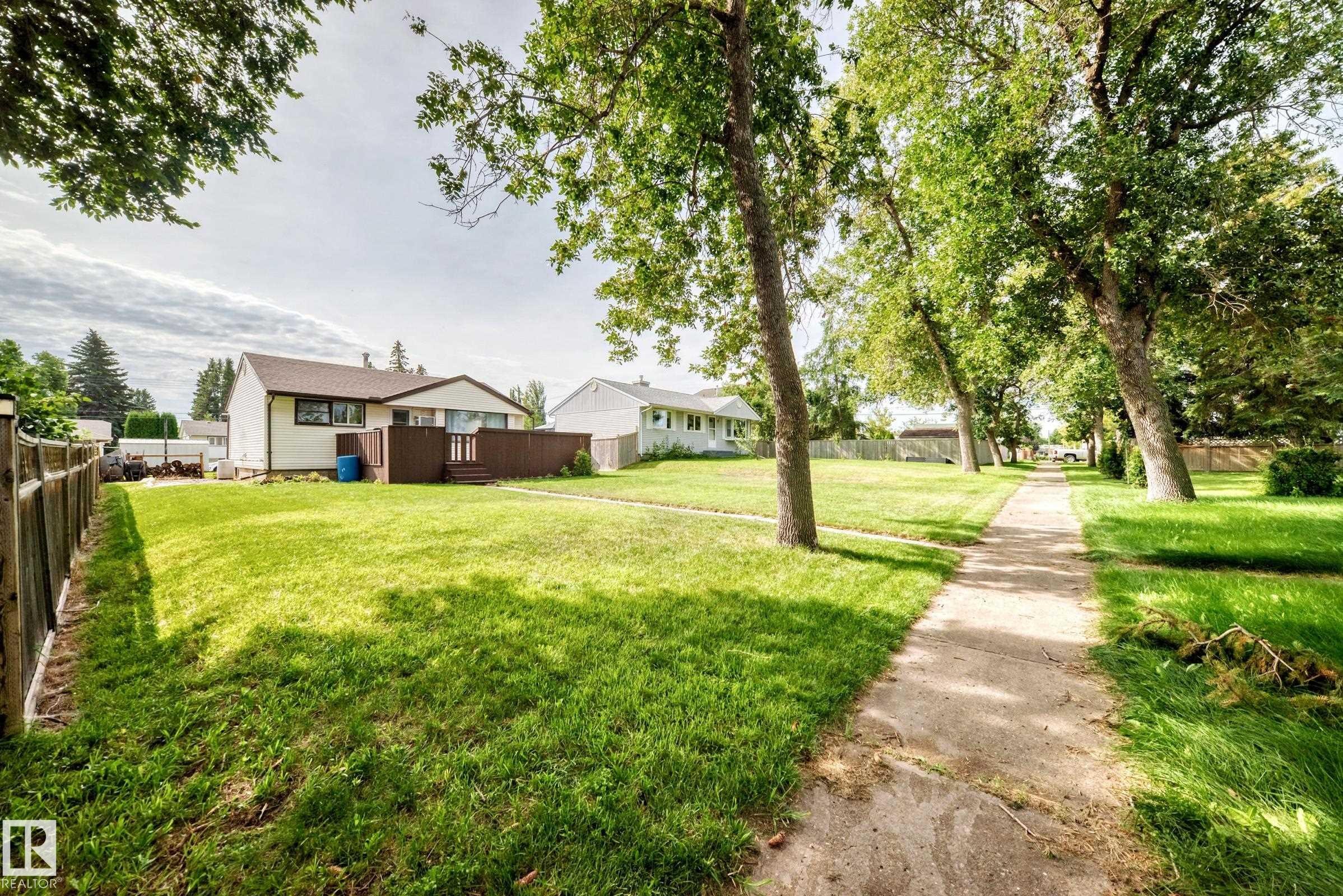 Expansive grassy yard with mature trees, a wooden privacy fence, and a concrete walkway - 50 Rocque, Fort Saskatchewan, AB - Outdoor