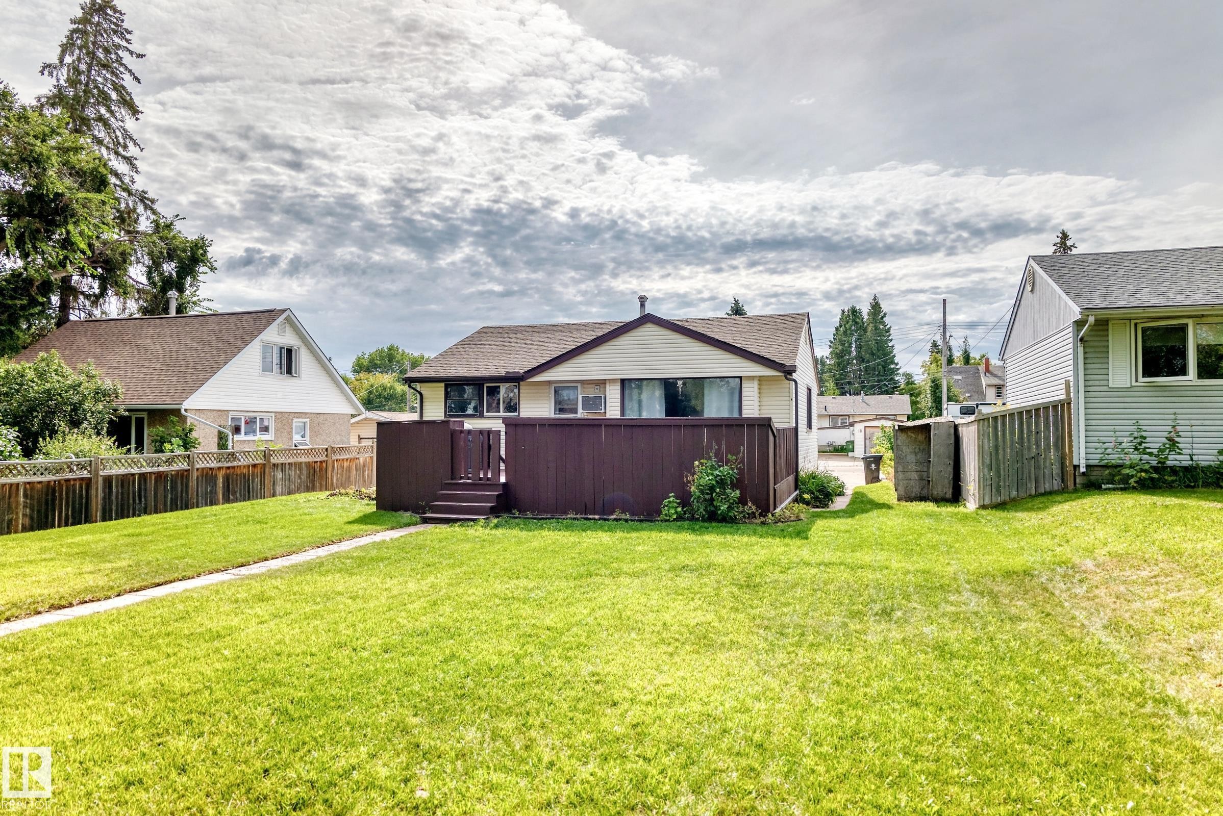 Expansive backyard featuring a manicured lawn, a brown privacy fence, and a raised wooden deck with steps - 50 Rocque, Fort Saskatchewan, AB - Outdoor