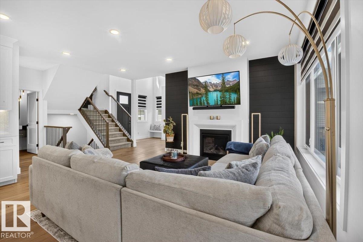 Wood-finish flooring throughout, a shiplap accent wall, fireplace with white mantel, recessed lighting, and a staircase with wood treads and metal balusters - 94 Harvest Crescent, Ardrossan, AB - Indoor Photo Showing Living Room With Fireplace