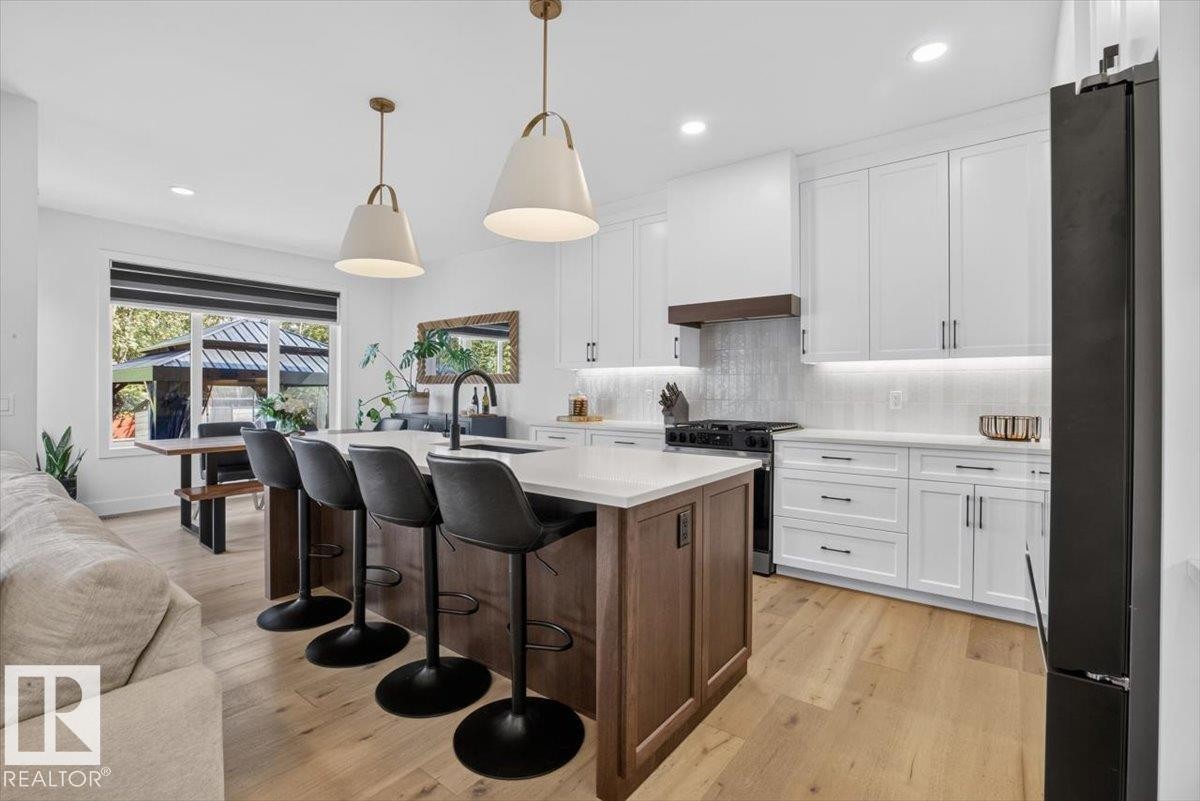 Gourmet kitchen with wood-finish flooring, white cabinetry, a large kitchen island, and under-cabinet lighting - 94 Harvest Crescent, Ardrossan, AB - Indoor Photo Showing Kitchen With Upgraded Kitchen