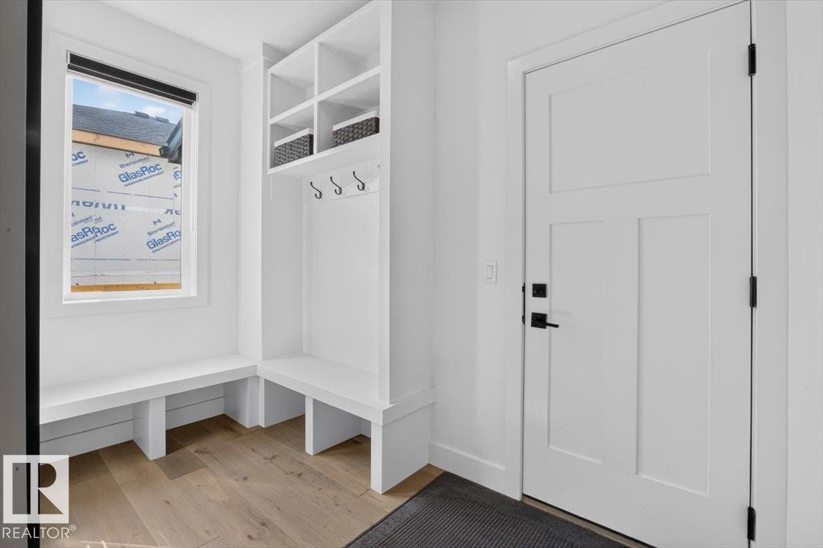 Built-in white storage bench, recessed shelving with coat hooks, white paneled door with matte black hardware, and wood-finish flooring - 94 Harvest Crescent, Ardrossan, AB - Indoor Photo Showing Other Room