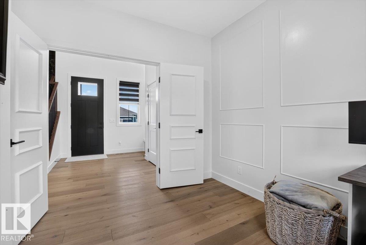 Light wood-finish flooring, white paneled accent wall, contemporary interior doors with matte black hardware, and an entryway with a dark-paneled door - 94 Harvest Crescent, Ardrossan, AB - Indoor Photo Showing Other Room