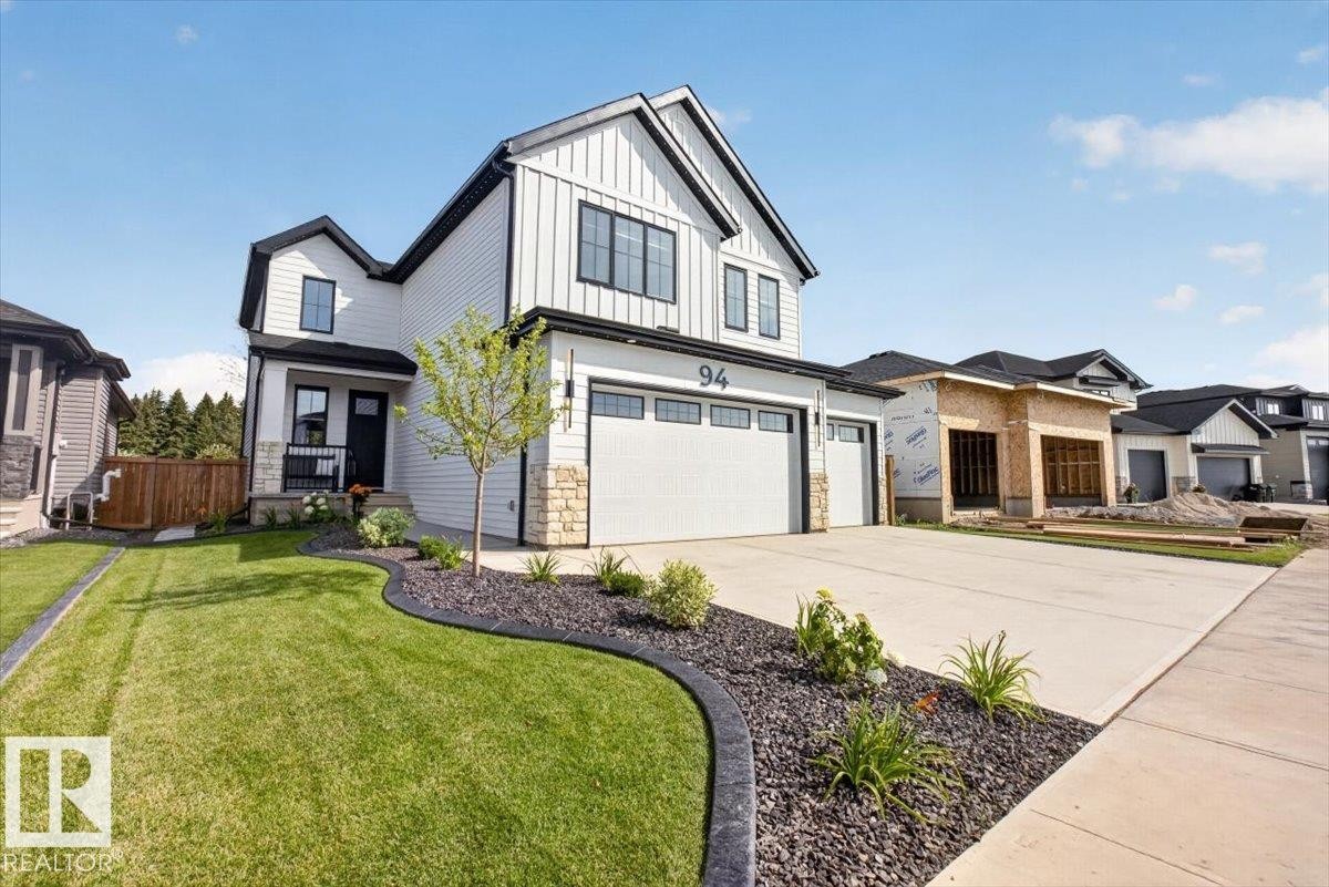Contemporary exterior featuring light-colored siding with dark trim accents, a two-car garage, and a concrete driveway - 94 Harvest Crescent, Ardrossan, AB - Outdoor