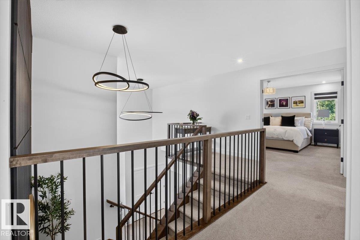 Contemporary hanging light fixtures, wood-finish and wrought iron stair railing, wood-paneled accent wall, and recessed lighting - 94 Harvest Crescent, Ardrossan, AB - Indoor Photo Showing Other Room