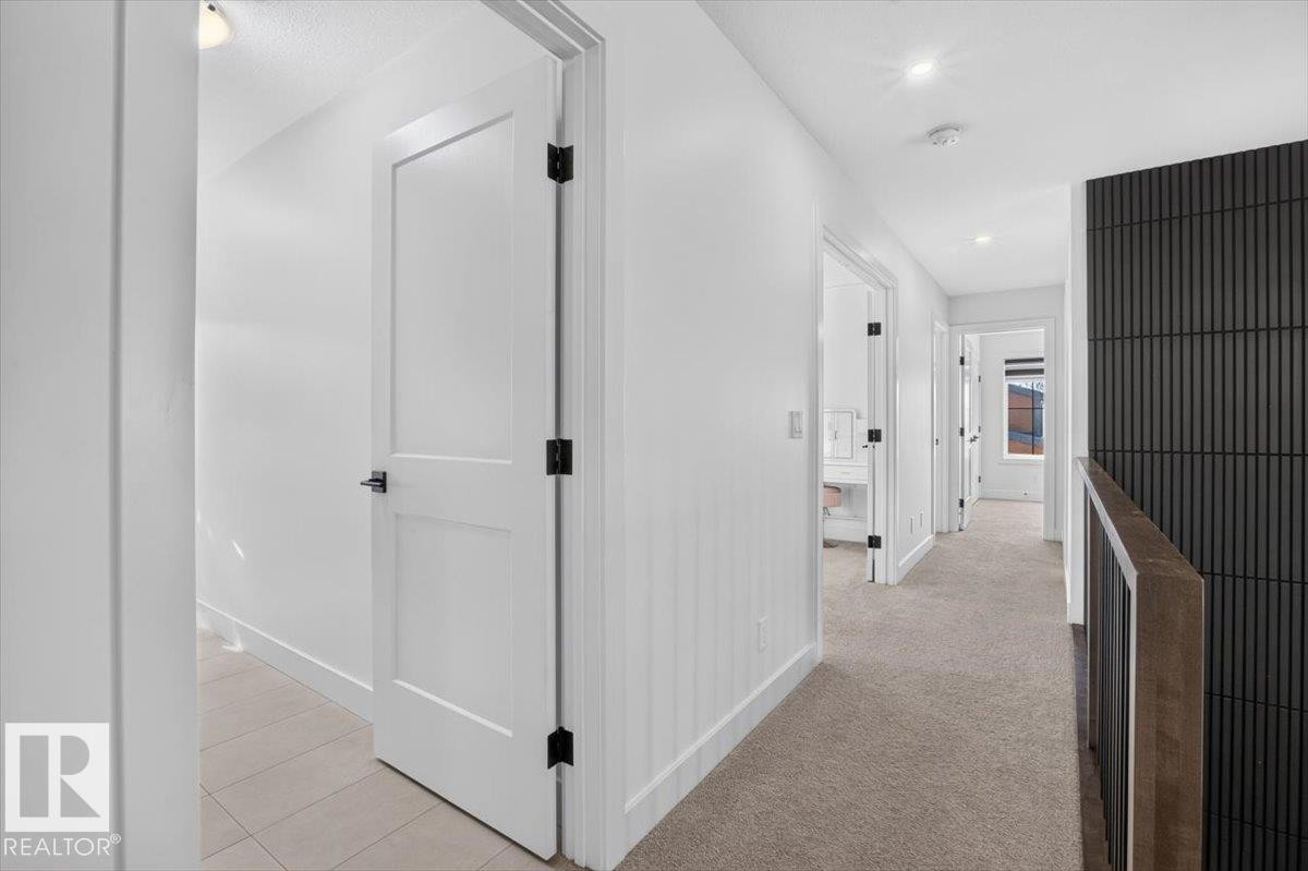 Hallway featuring neutral-toned carpeting, white interior doors with matte black hardware, and a textured dark accent wall - 94 Harvest Crescent, Ardrossan, AB - Indoor Photo Showing Other Room