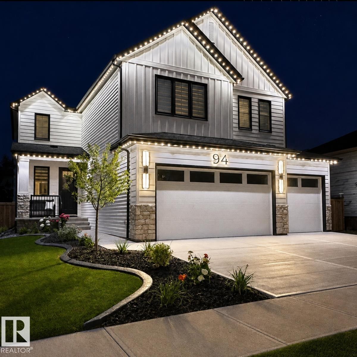 White siding exterior with board and batten accents, stone detailing, a two-car garage, and established landscaping - 94 Harvest Crescent, Ardrossan, AB - Outdoor With Facade