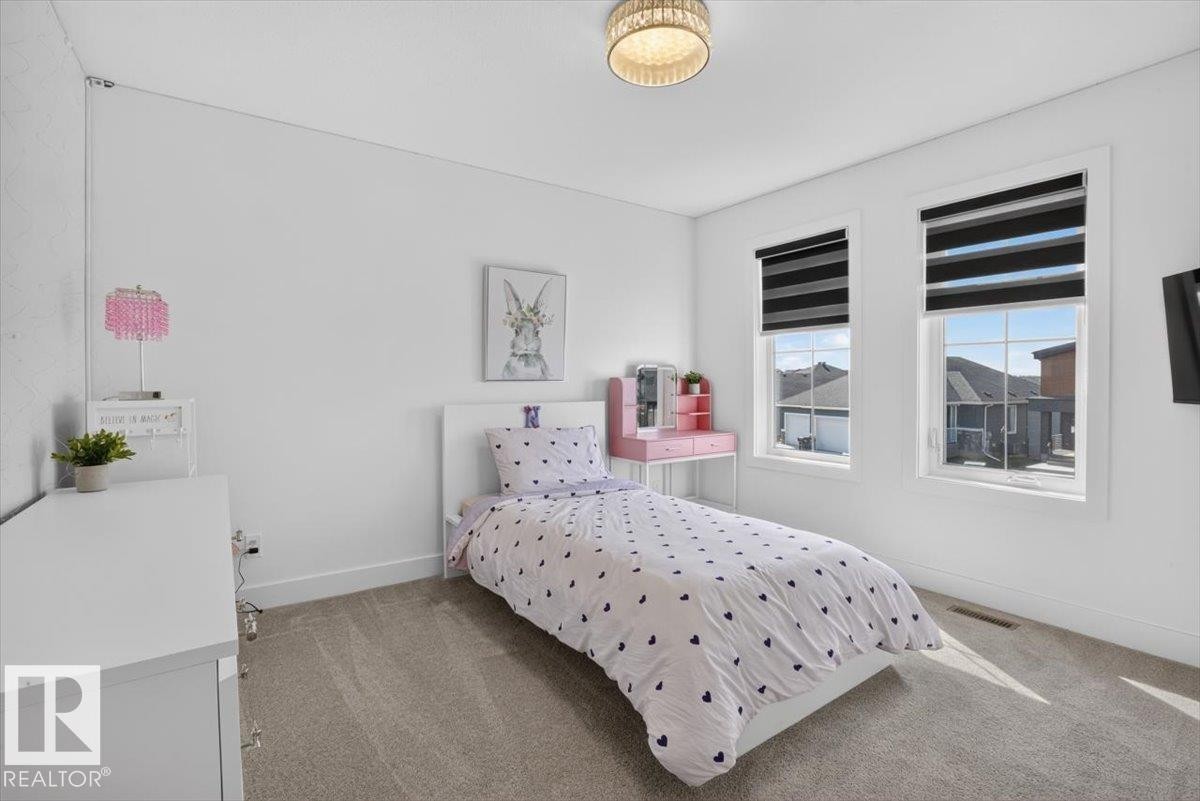 Carpeted room with two large windows, roller shades, and a decorative ceiling light fixture - 94 Harvest Crescent, Ardrossan, AB - Indoor Photo Showing Bedroom